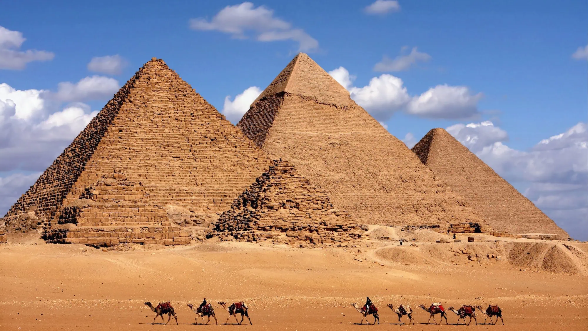 Panoramic view of the three Pyramids of Giza with a camel caravan crossing the desert in front of them, the fourth-dynasty royal tombs on the plateau west of Cairo.
