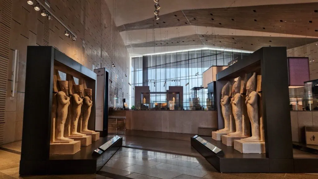 Interior gallery of the Grand Egyptian Museum in Giza showing ancient Egyptian artifacts and statues displayed in a modern museum hall.