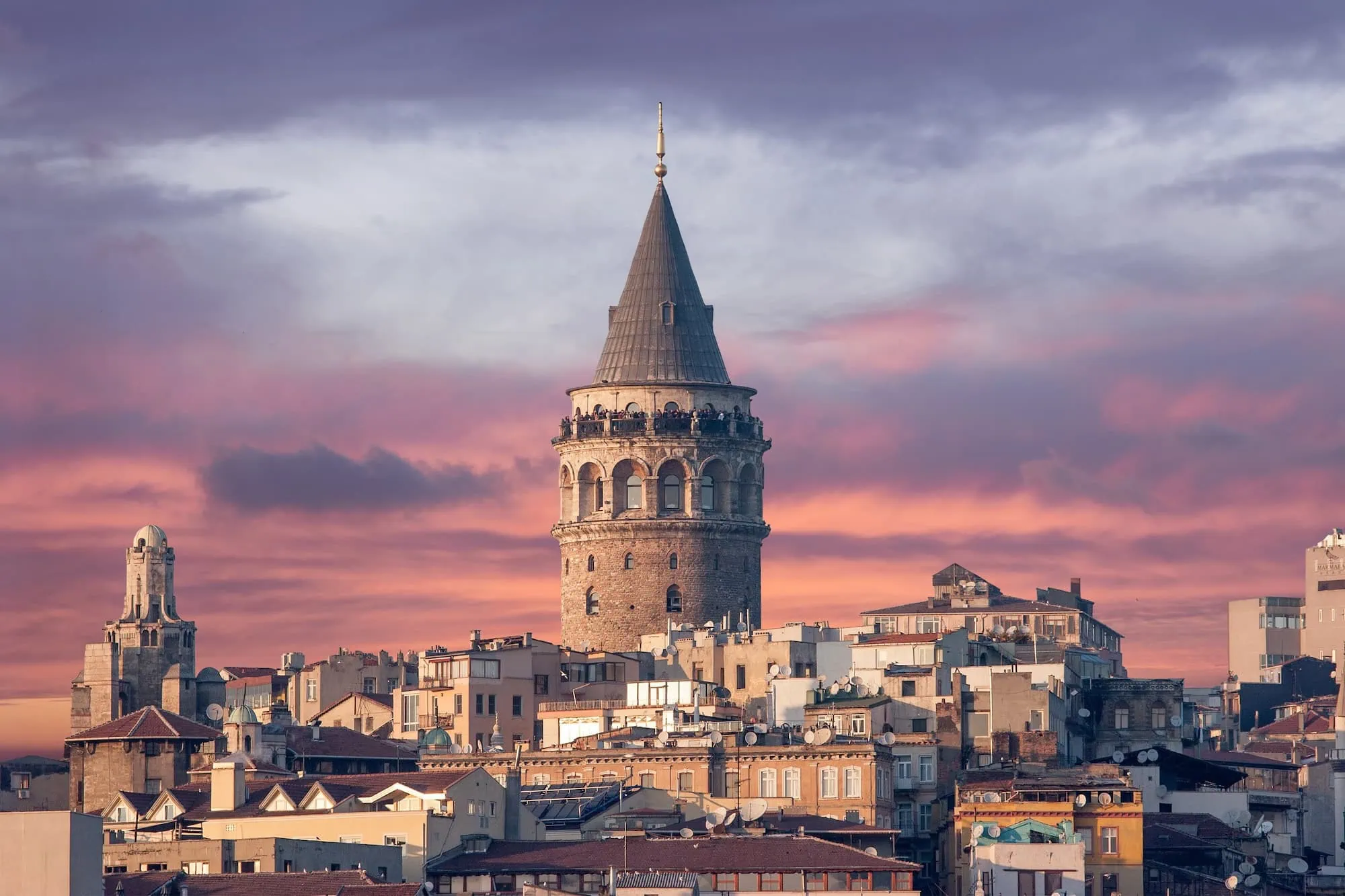 Galata Tower at sunset with dramatic purple and orange sky over Istanbul cityscape