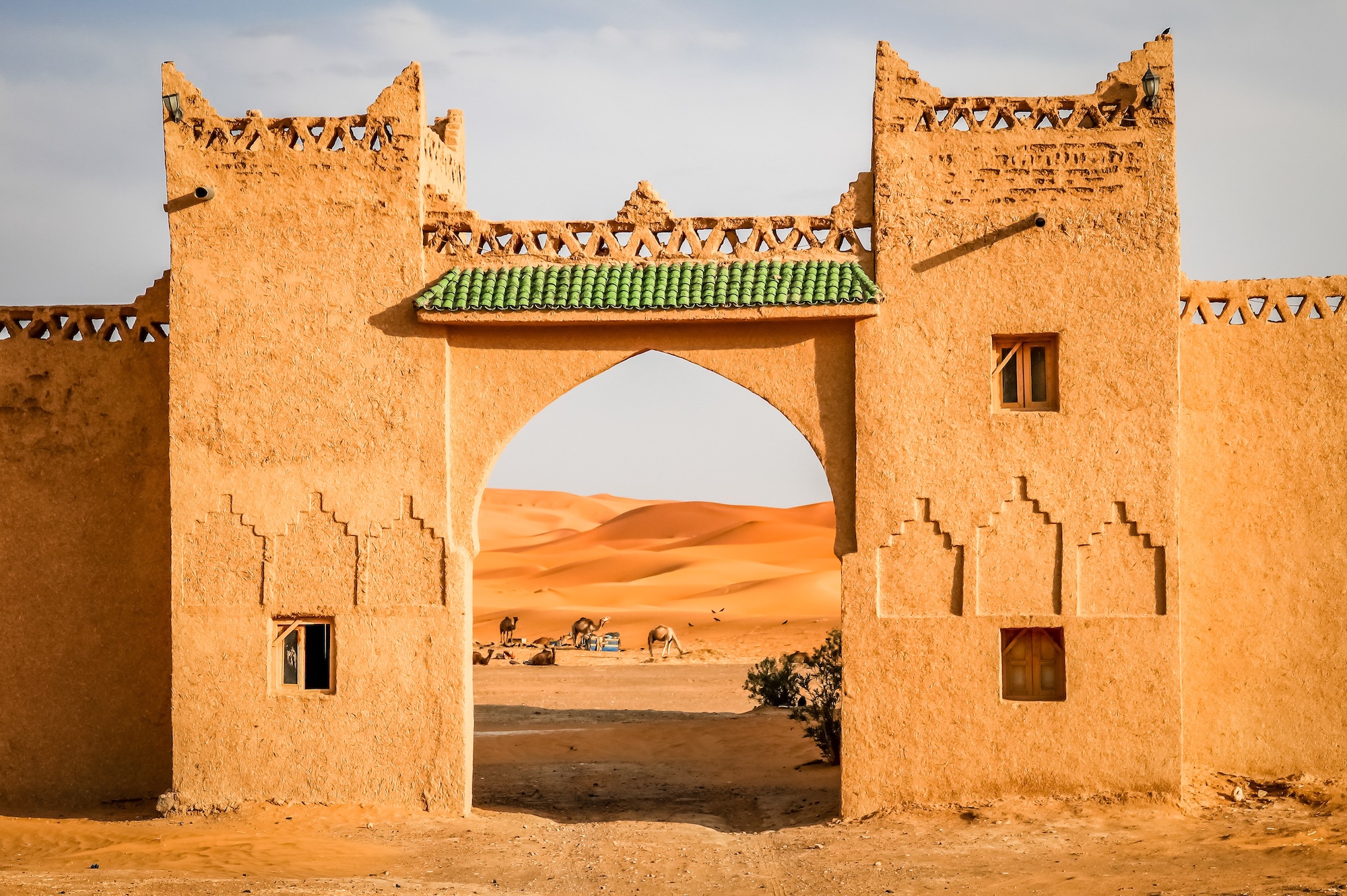 Traditional Moroccan gate framing view of Sahara desert sand dunes with resting camels