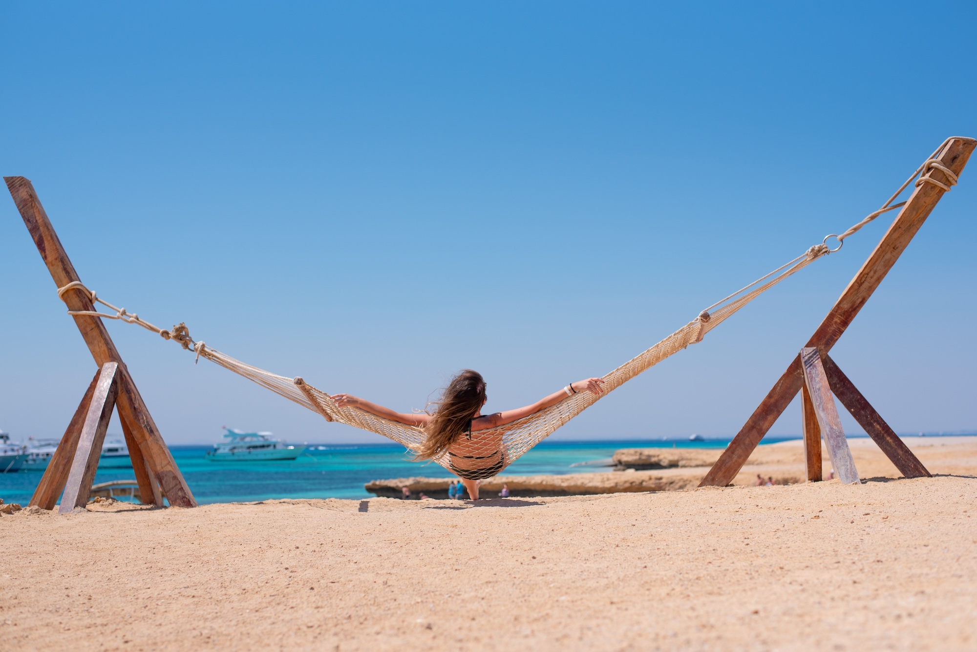 Woman relaxing in hammock on Orange Bay beach with turquoise water and boats
