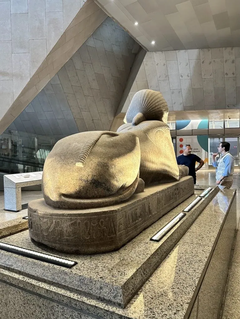 Guide and tourist standing before a granite sphinx from the Great Temple of Amun