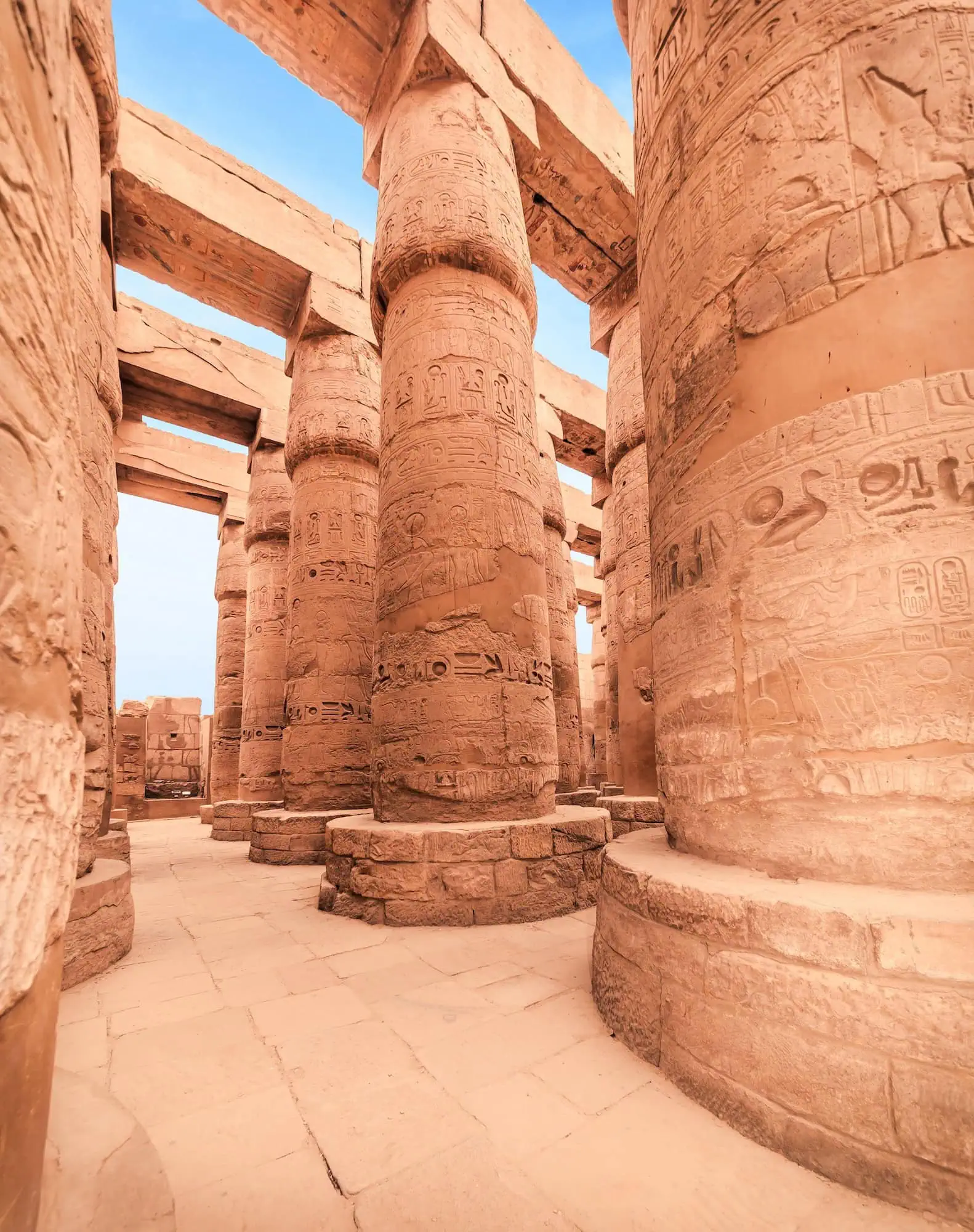The Great Hypostyle Hall at Karnak Temple in Luxor with massive sandstone columns covered in hieroglyphic carvings, photographed from ground level looking upward through the column forest.