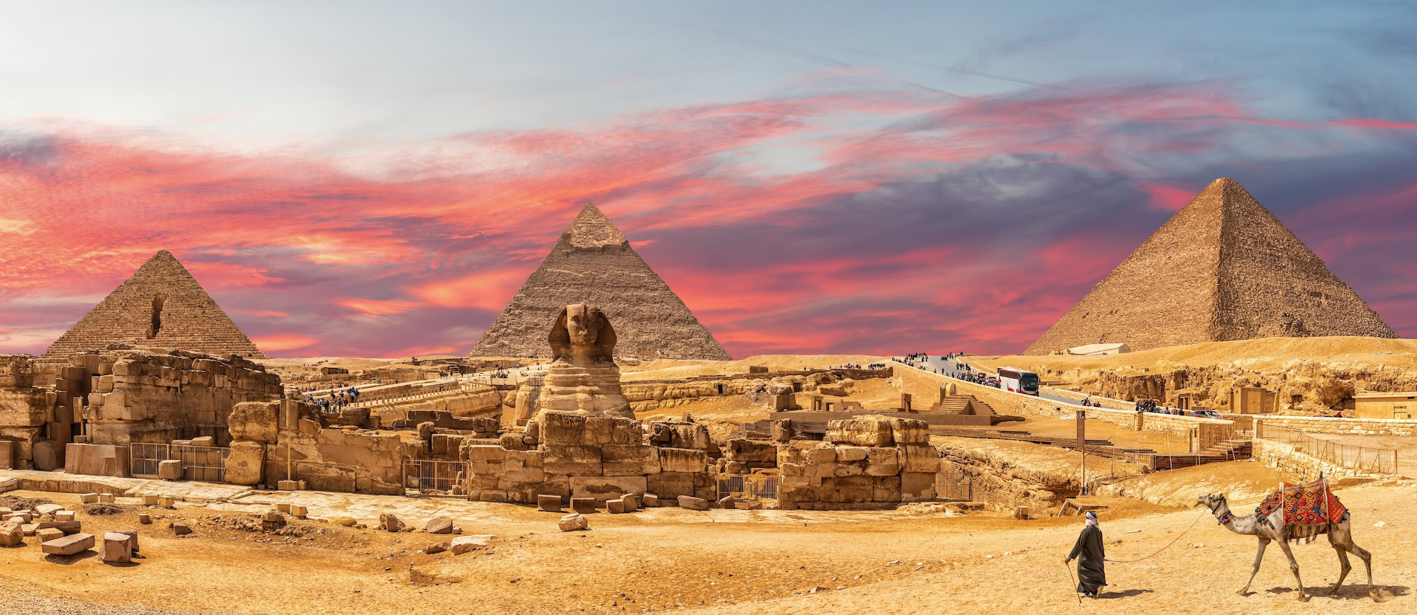 Great Pyramids of Giza and Sphinx with tourists and camel in desert landscape