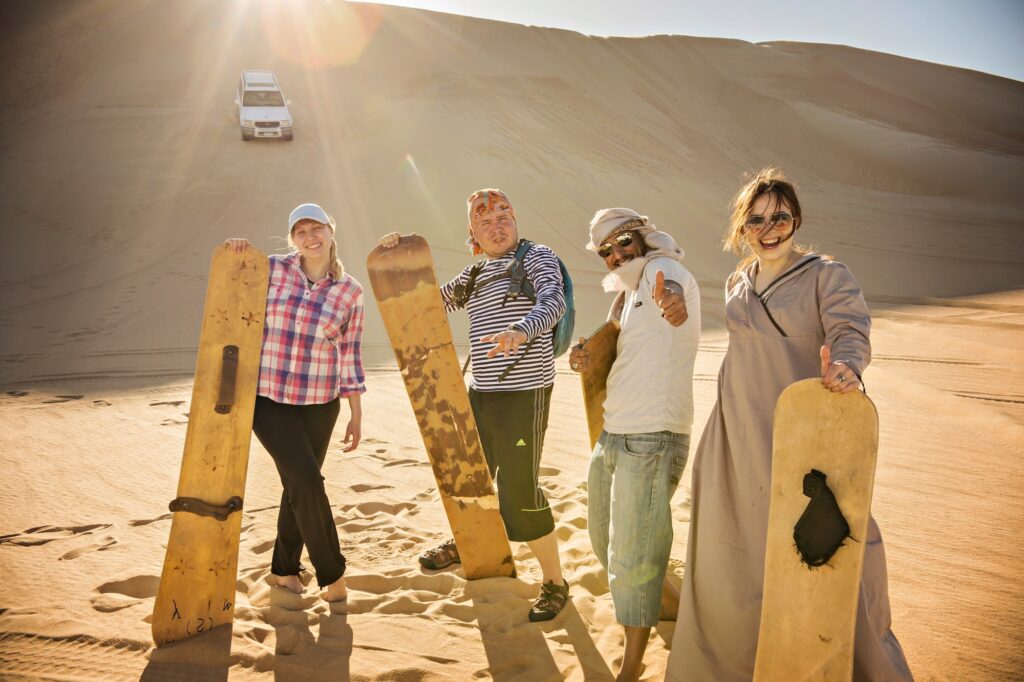 Happy young group holding sand boards on Sahara dunes near Siwa Oasis