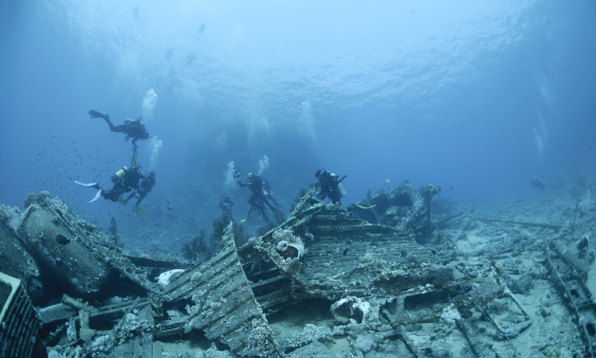 Scuba divers exploring underwater shipwreck debris at diving site