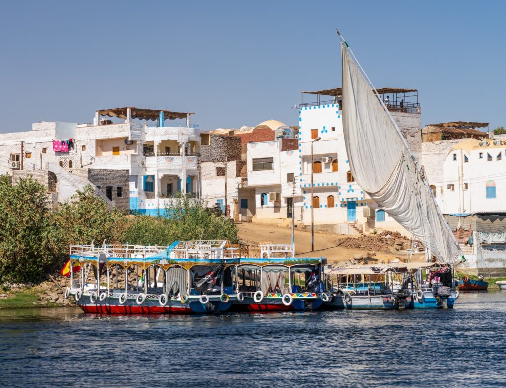Homes line the shores of Nile on Elephantine island with ferry boats and cruise boats docked alongside in Aswan