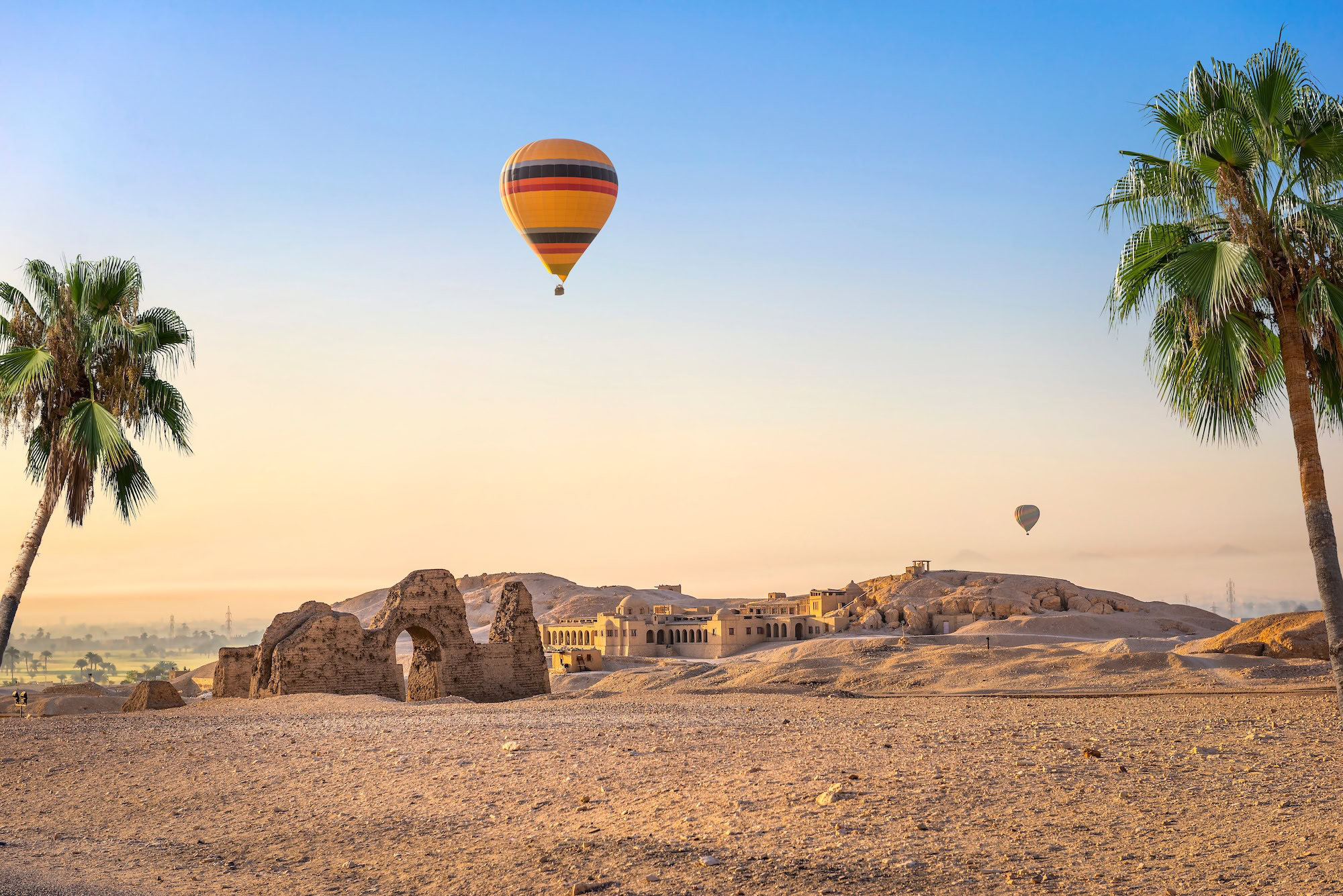 Paesaggio egiziano con mongolfiera, palme e rovine antiche sotto il cielo sereno del deserto