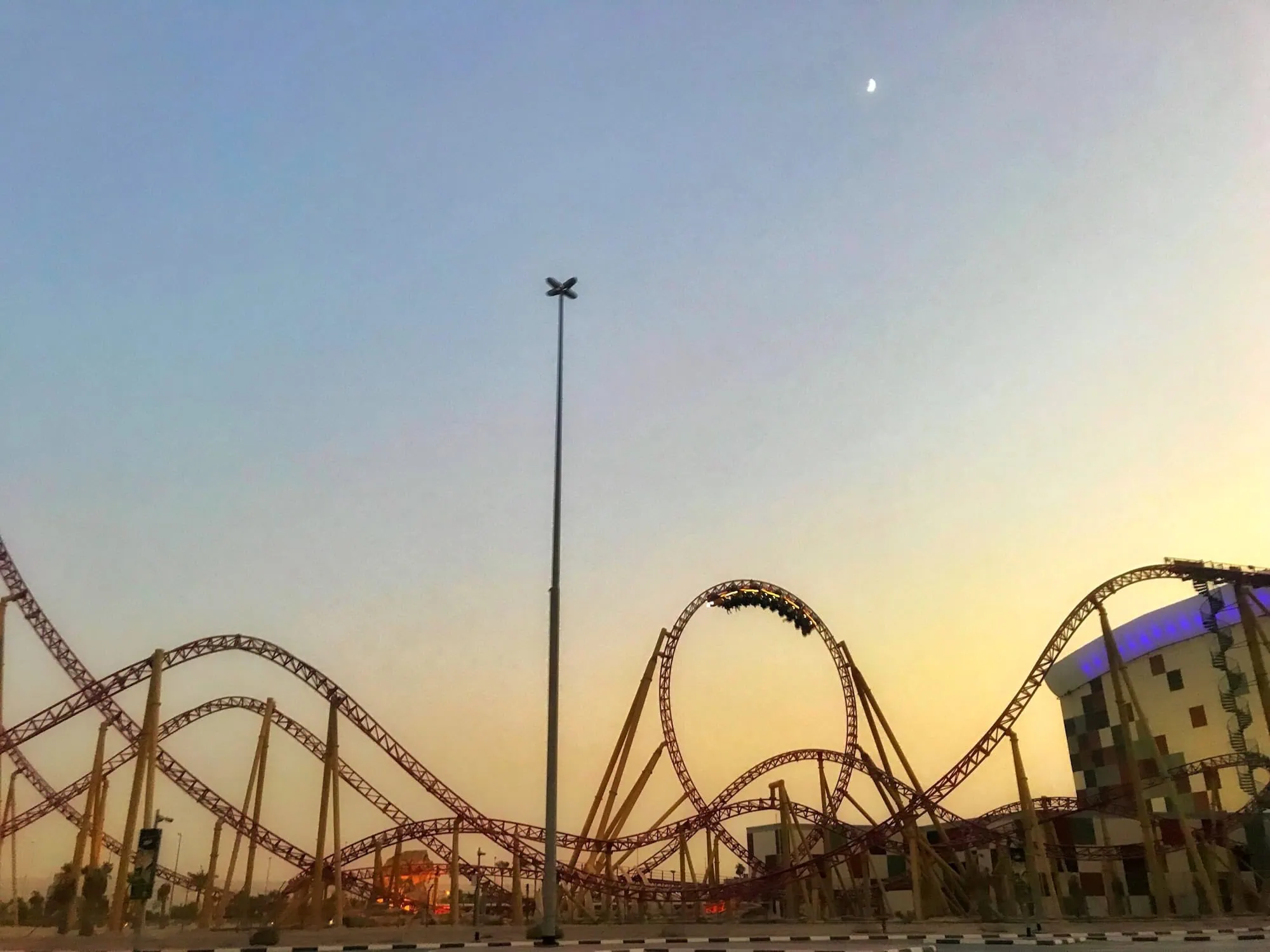 Dramatic sunset view of roller coaster tracks with loops against colorful sky at IMG Worlds of Adventure
