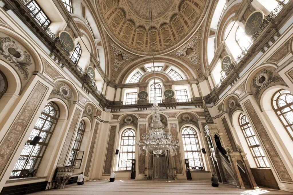 Dolmabahce Mosque interior with worshippers praying beneath ornate arches and chandeliers Istanbul