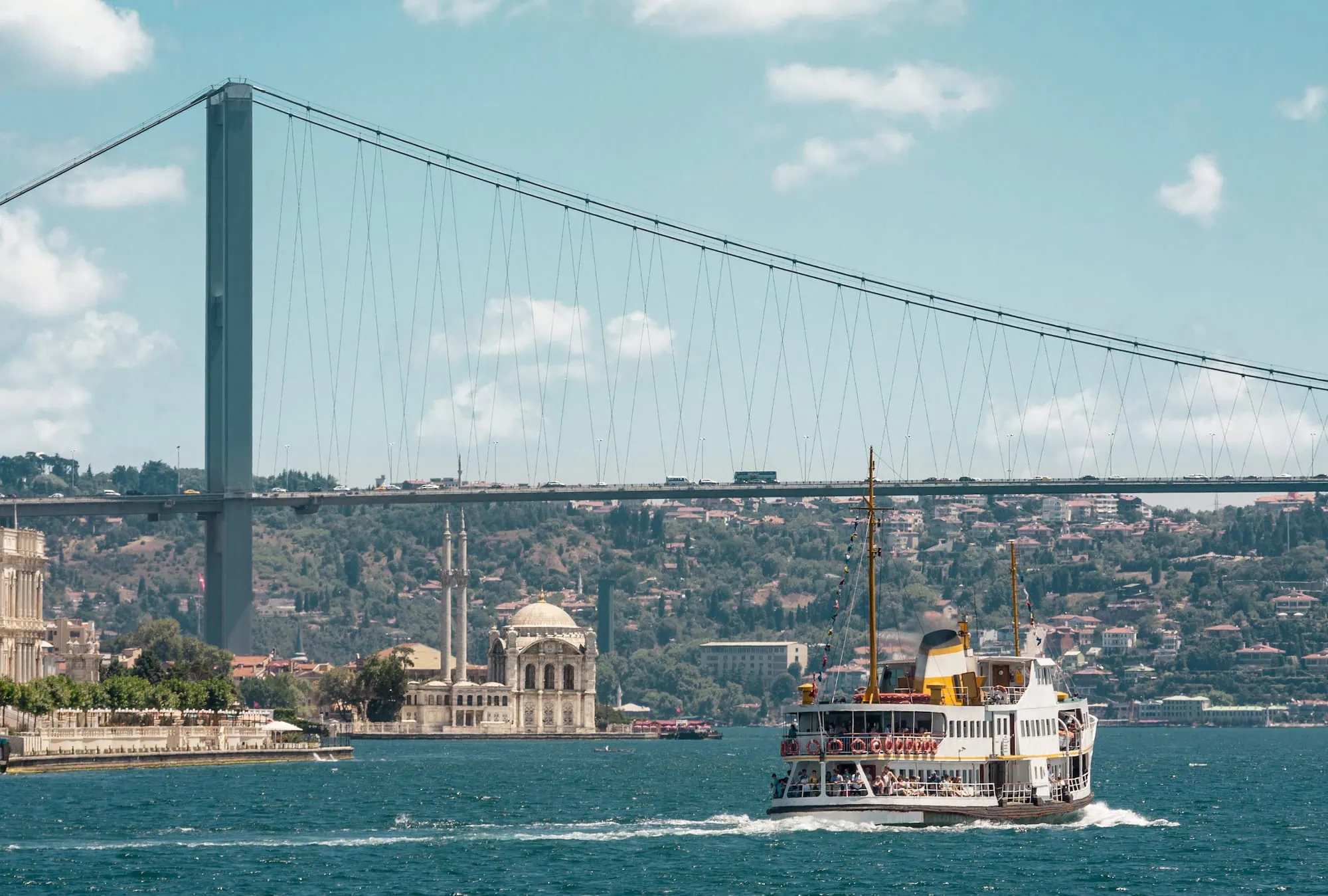Ferry boat sailing on Bosphorus strait with suspension bridge and mosque in background