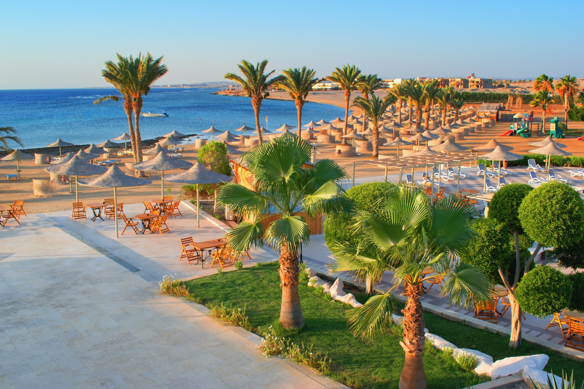 Serene beach resort with dining area, palm trees, umbrellas and loungers overlooking the sea