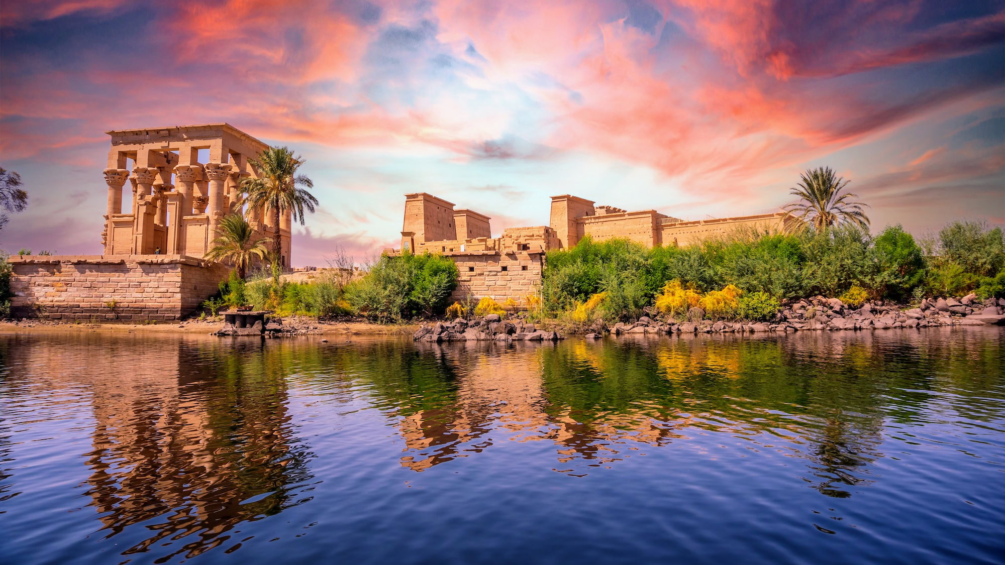 Philae Temple complex reflected in water with palm trees and ancient columns