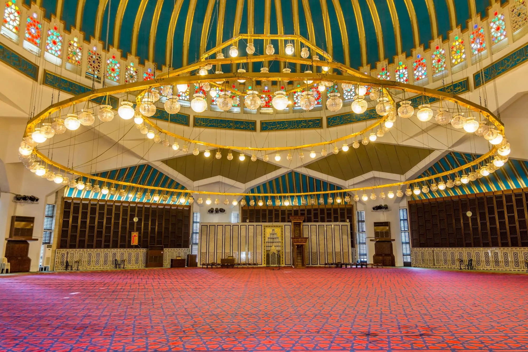 Interior de uma mesquita com tapetes, candelabro e janelas de vitral colorido