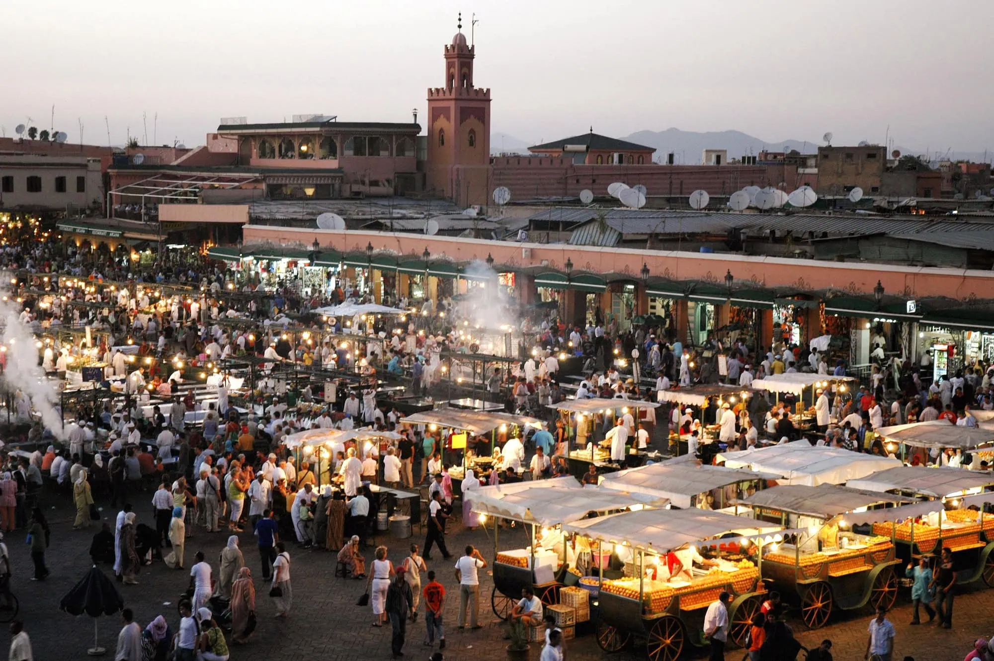 Bustling Jemaa el-Fna square in Marrakech at evening time with crowds, food stalls and mosque minaret