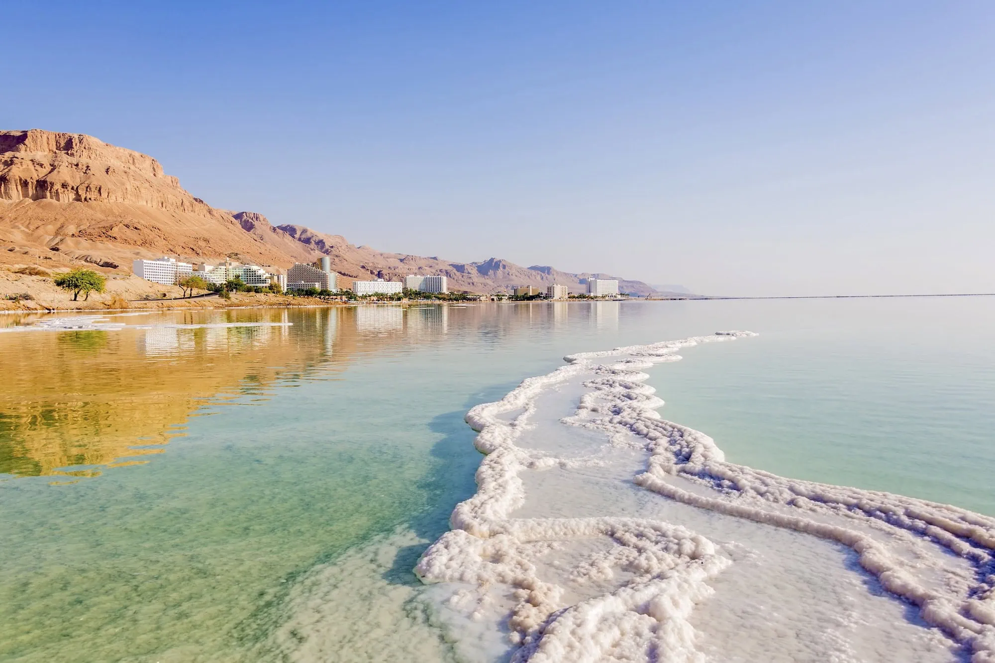 Dead Sea coastline in Jordan showing white salt deposits with hotel complexes and desert mountains