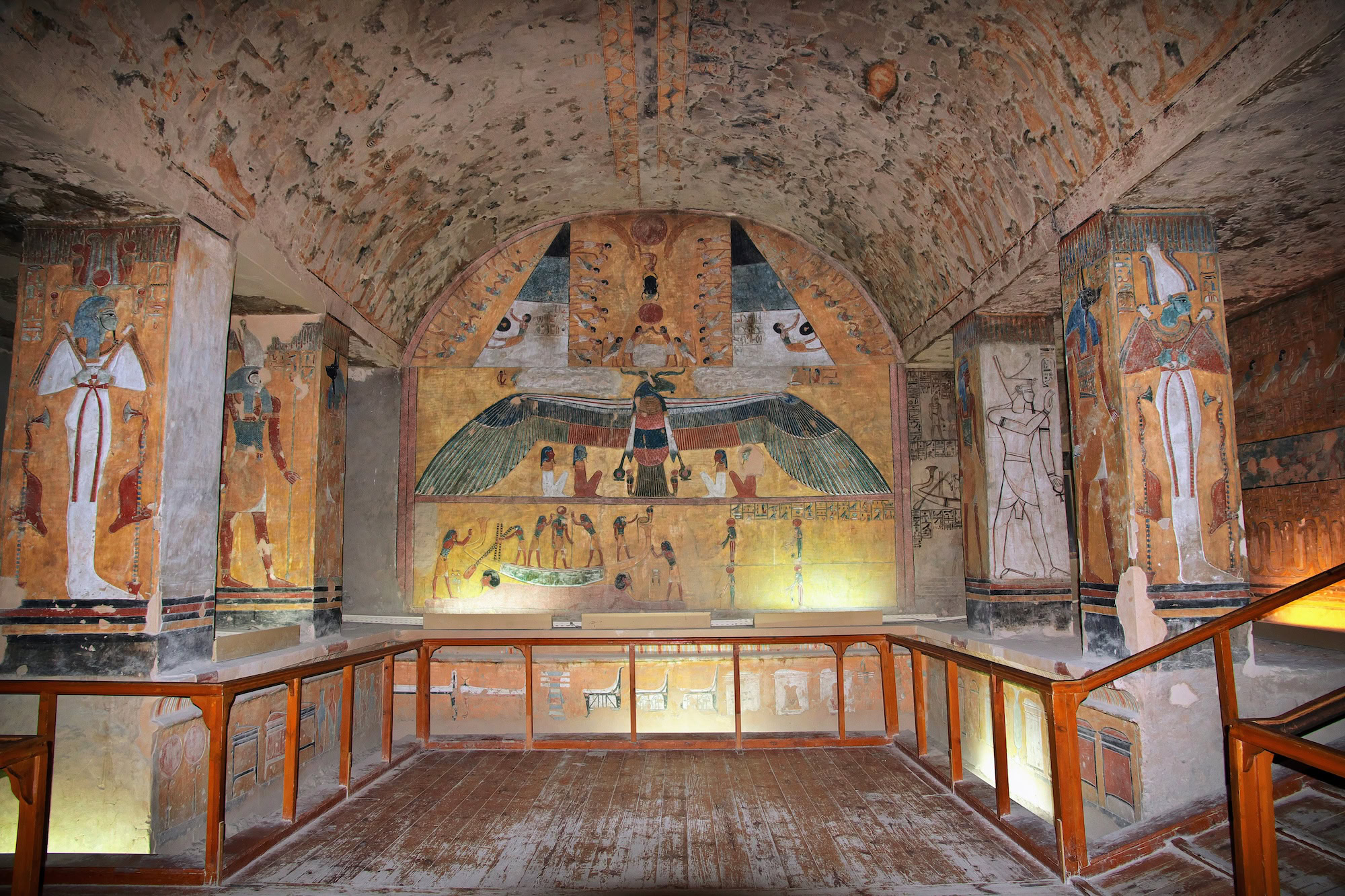 Ancient Egyptian tomb chamber with colorful wall paintings, hieroglyphics, and winged goddess decorations