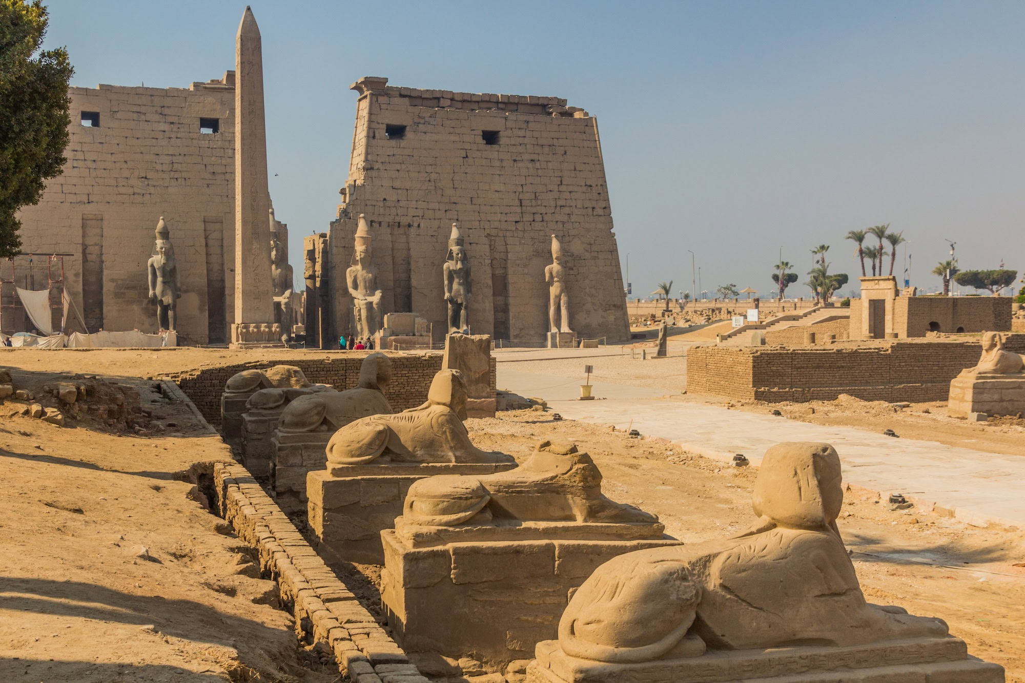 Ancient Egyptian Luxor Temple with sphinx statues, obelisk, and tourists exploring the historic site