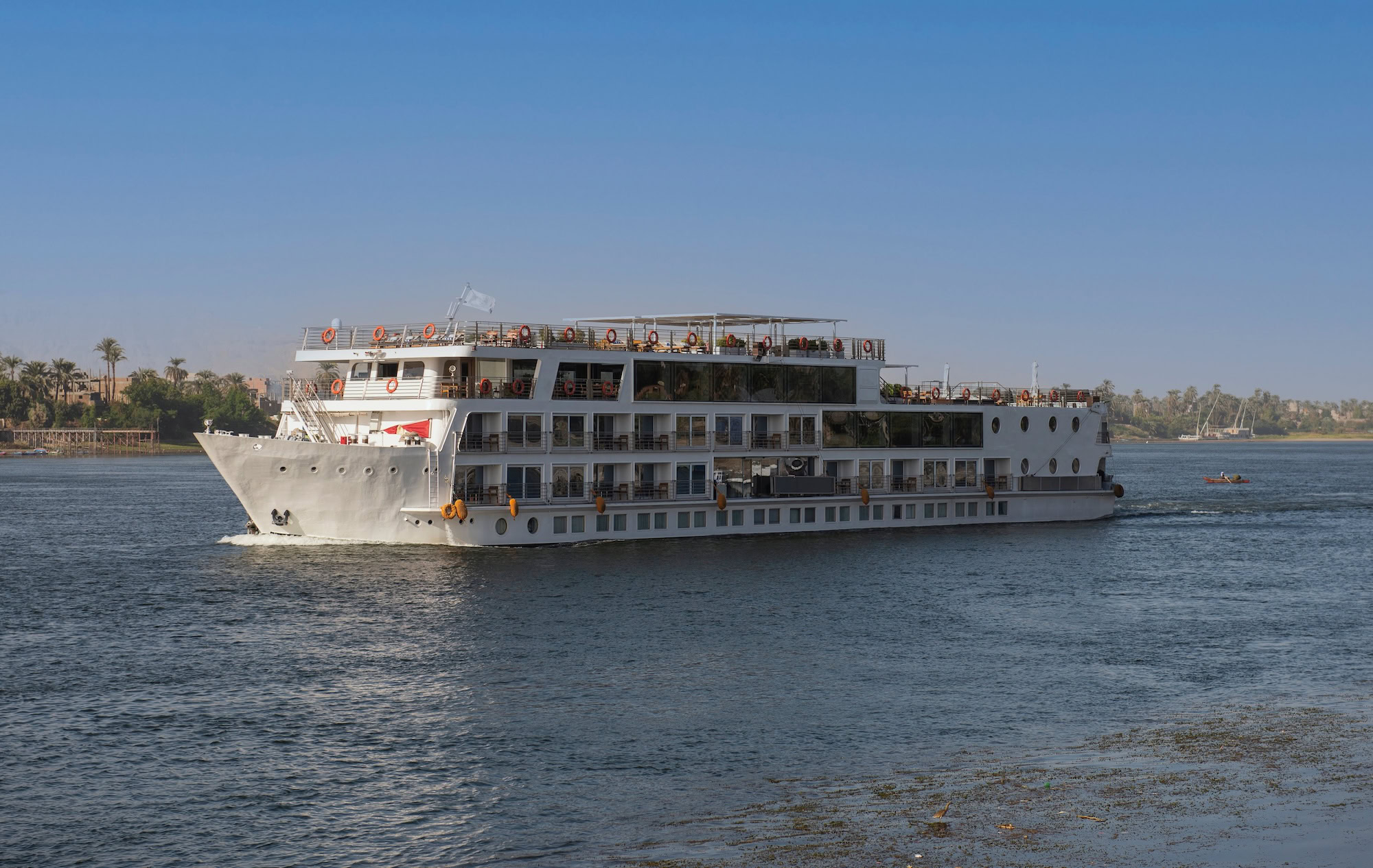 Nile River cruise ship near palm-lined shore with passengers on deck