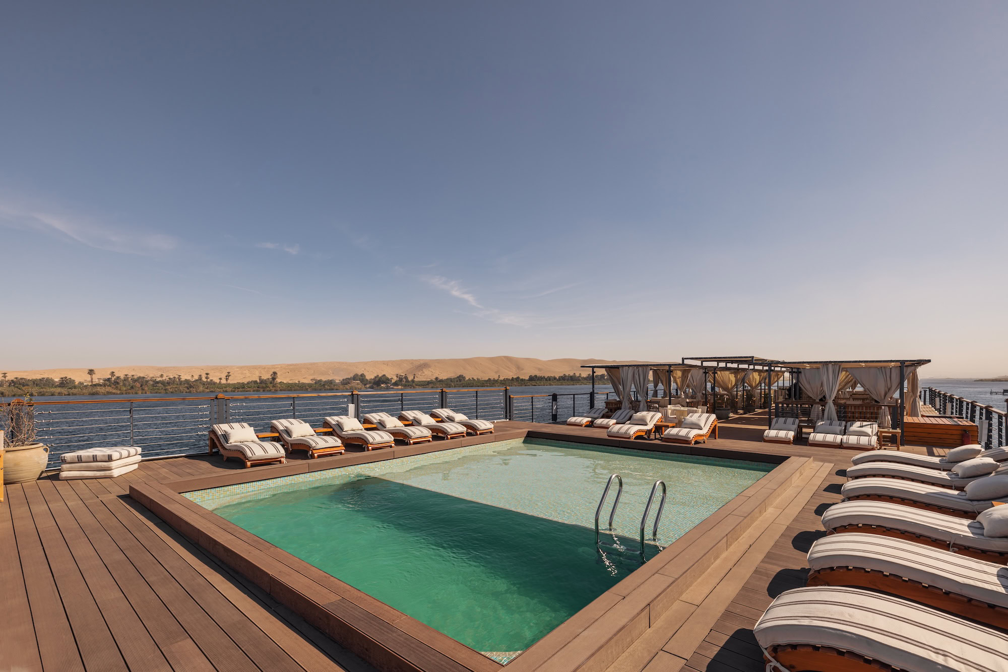 Luxury Nile River cruise ship deck with swimming pool, sun loungers, and wooden decking overlooking the river