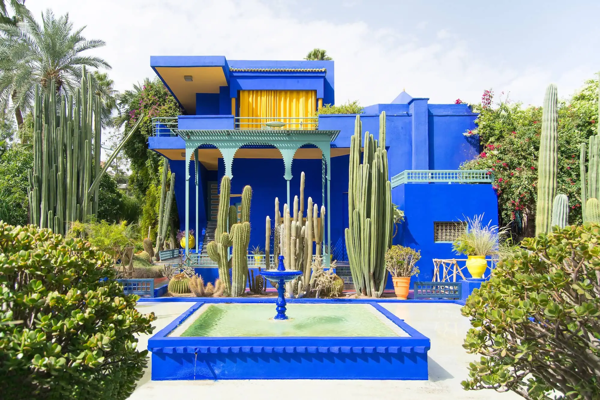 Majorelle Garden's iconic blue buildings and fountain surrounded by cacti and tropical vegetation