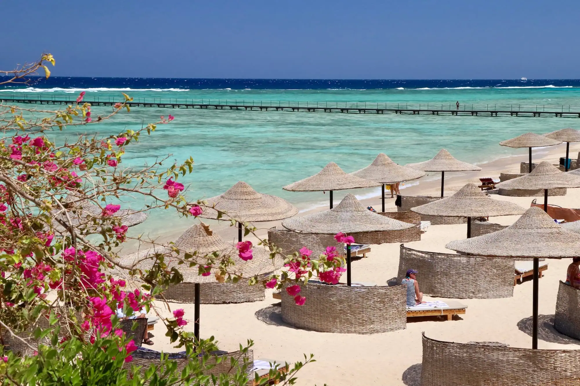 Beautiful Red Sea beach in Marsa Alam with turquoise waters, traditional umbrellas, and pink bougainvillea