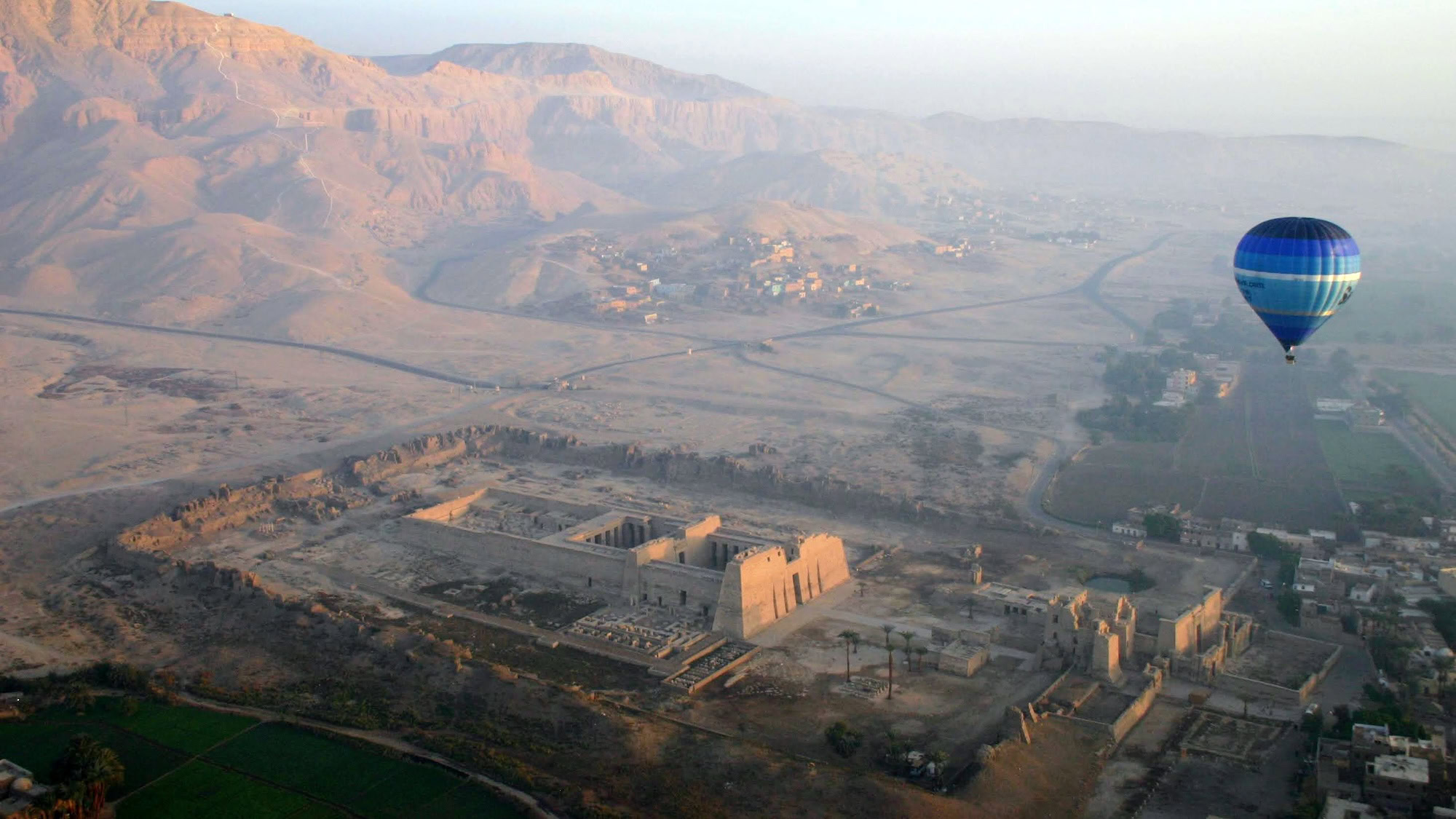 Aerial view of Valley of the Kings archaeological site with hot air balloon and ancient temples