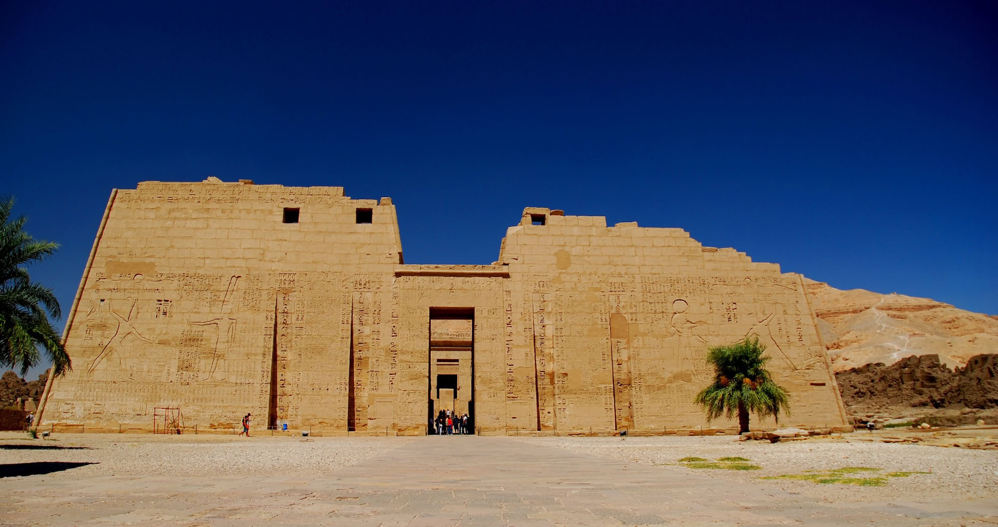Turistas visitando el templo de Medinet Habu con palmeras y jeroglíficos
