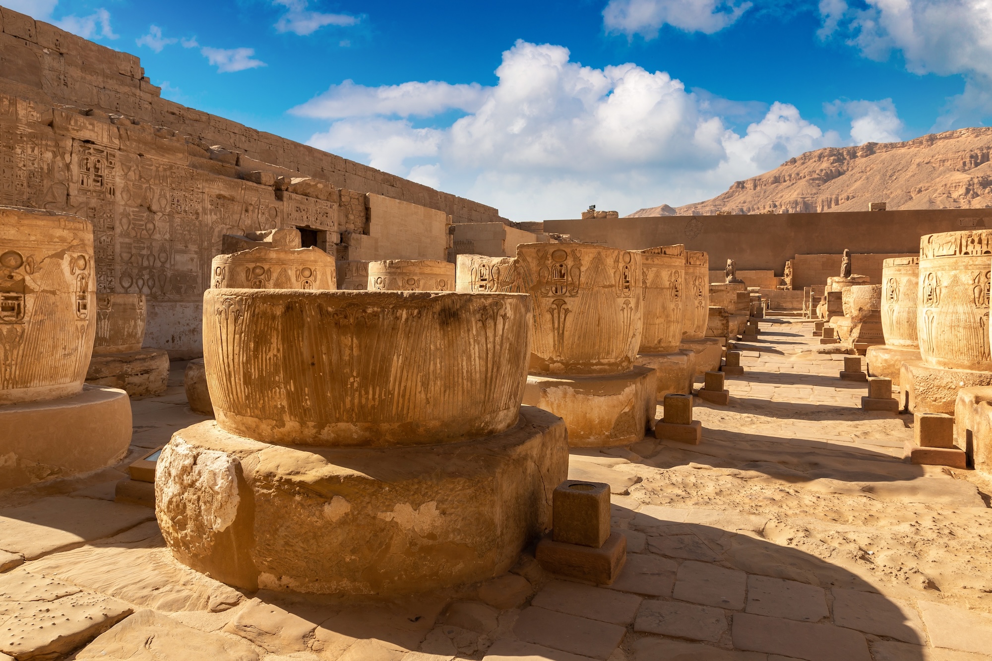 Ancient Egyptian temple columns with hieroglyphic carvings against desert cliffs