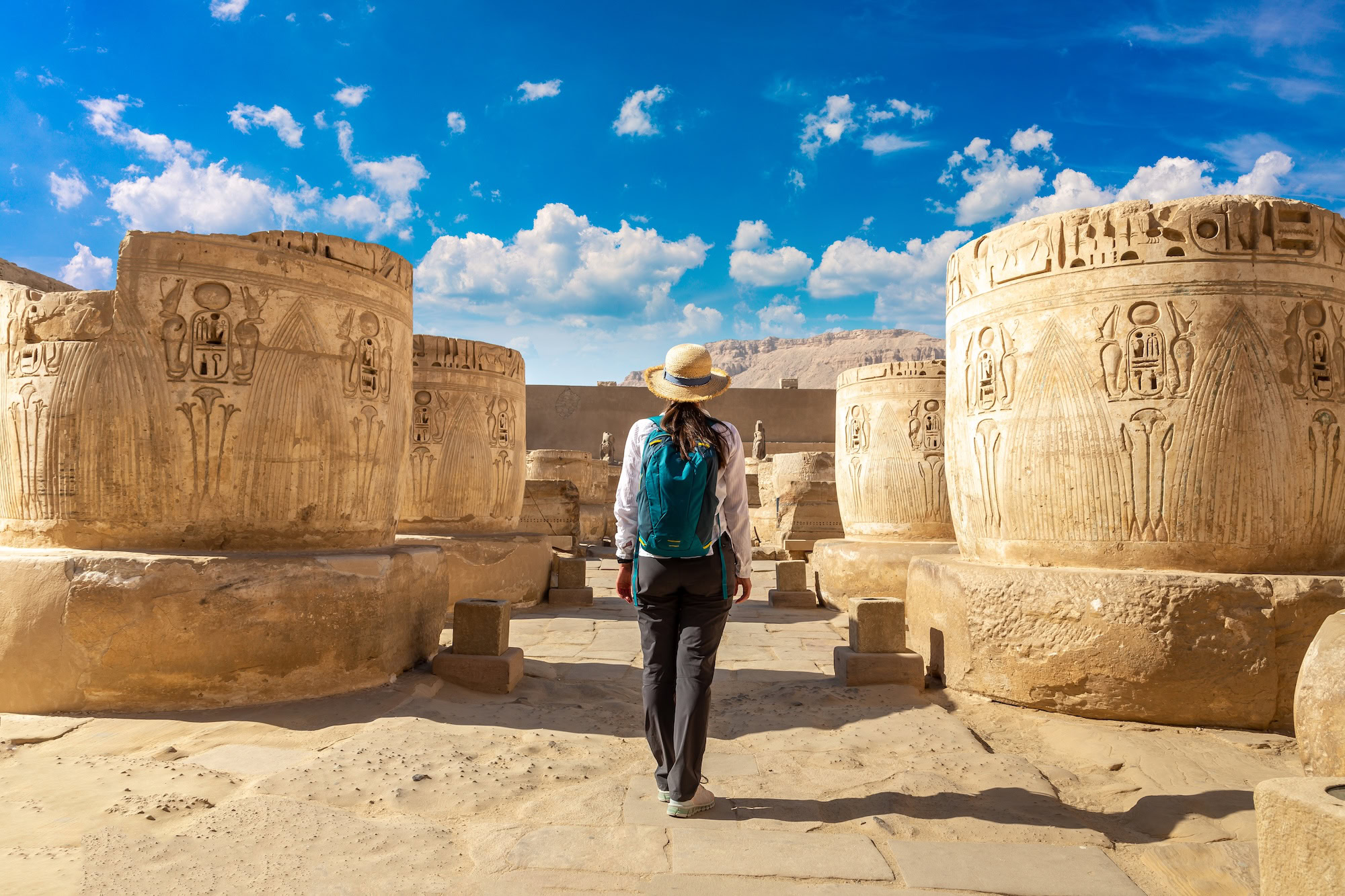 Turista com mochila explorando templo antigo egípcio com colunas e hieróglifos