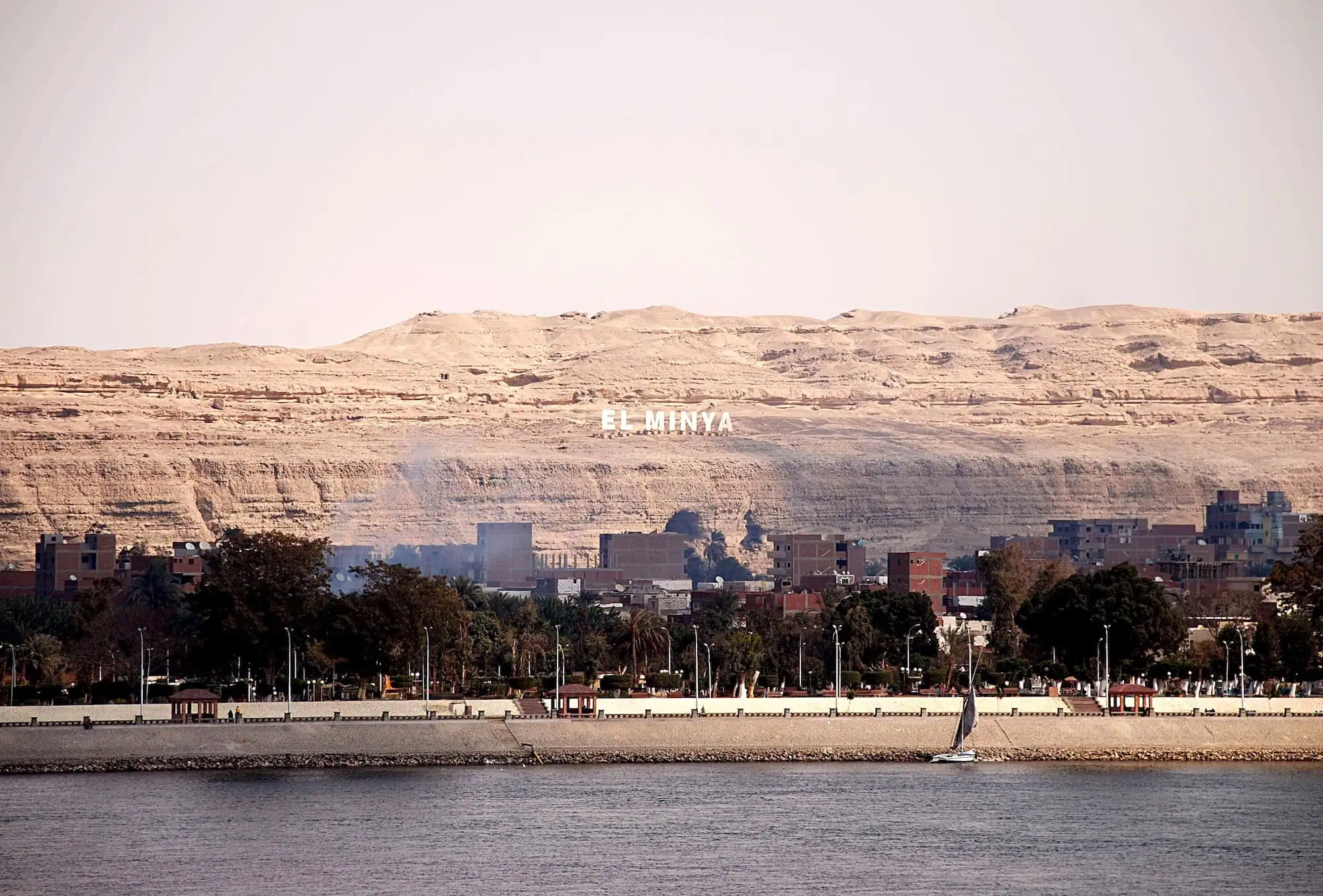 Minya waterfront with sailboat on river, palm trees and cliffs