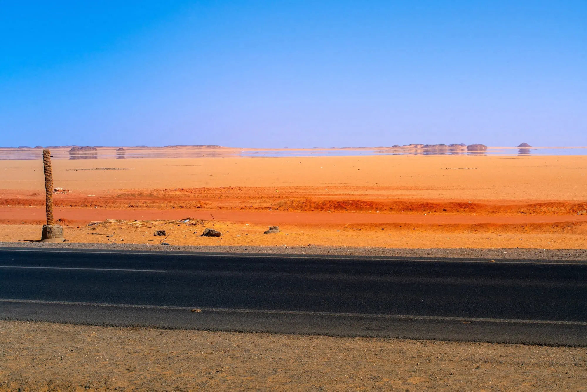 Shimmering mirage and heat haze rising off an empty desert road in Egypt under intense summer sun, illustrating the conditions a private Egypt all-inclusive itinerary is paced around.