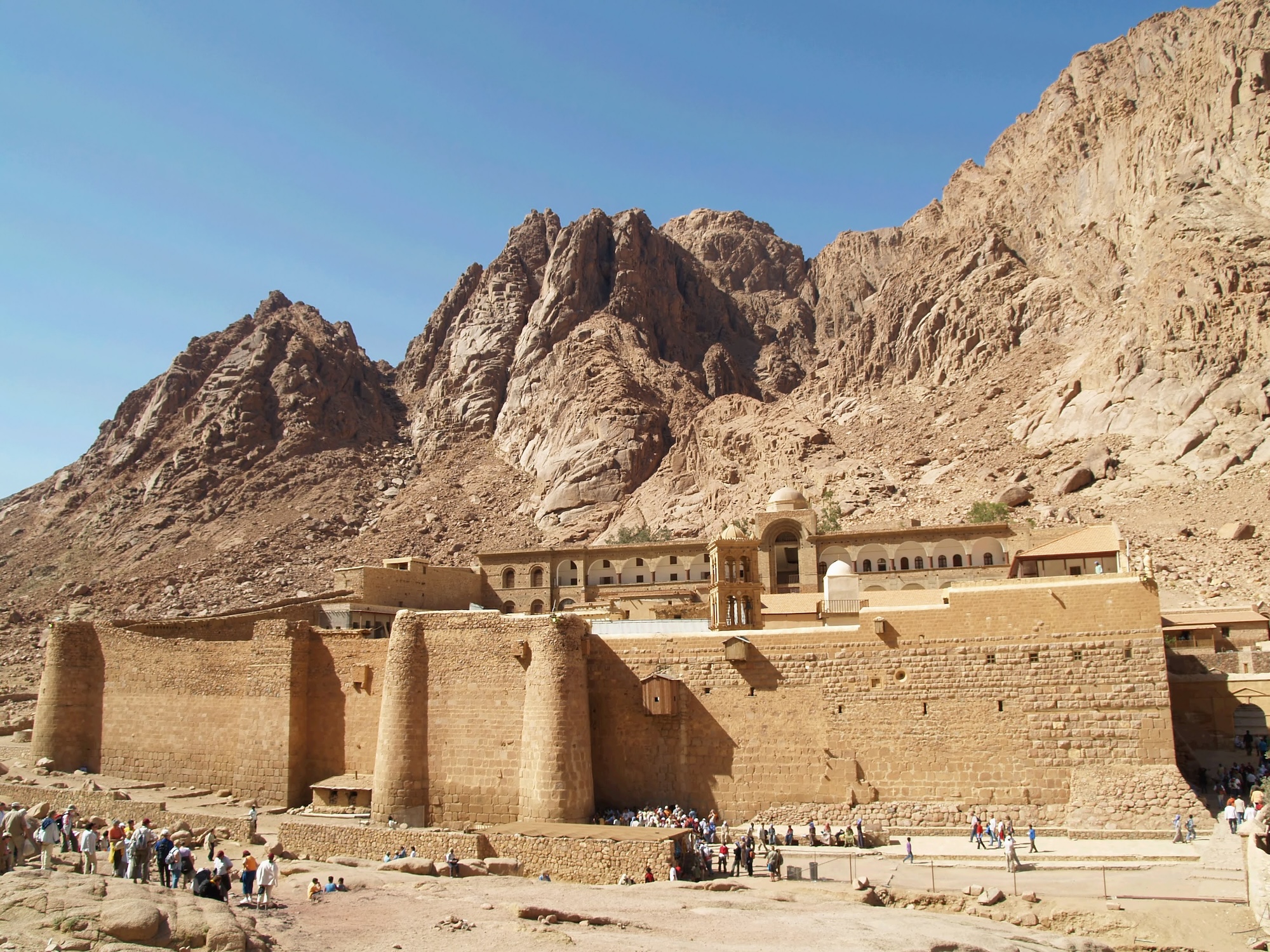 Tourists visiting Saint Catherine's Monastery with ancient stone walls and desert mountains in background