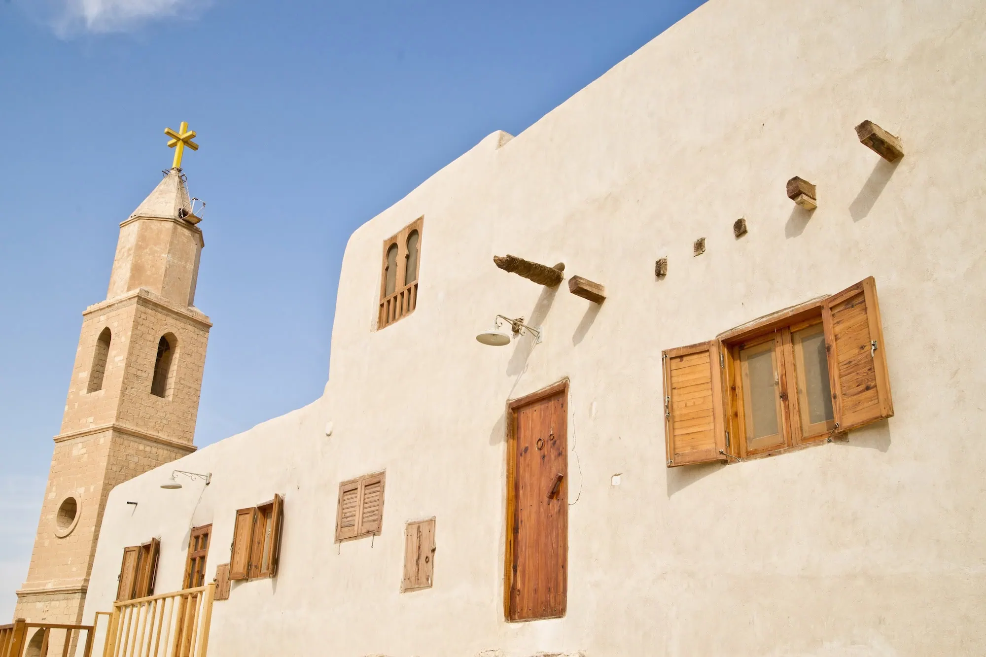 White monastery buildings with bell tower and golden cross against blue sky