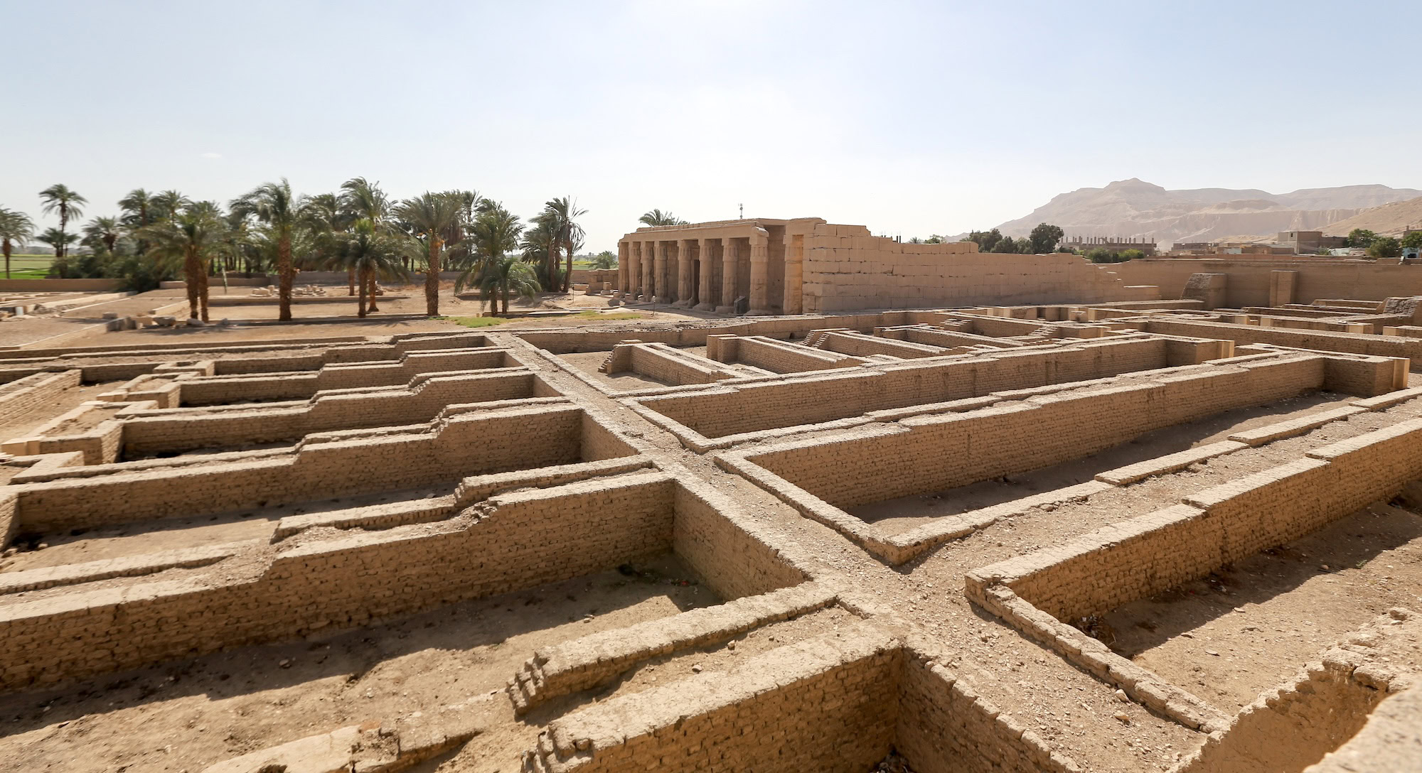 Ancient Egyptian temple ruins with palm trees and desert mountains