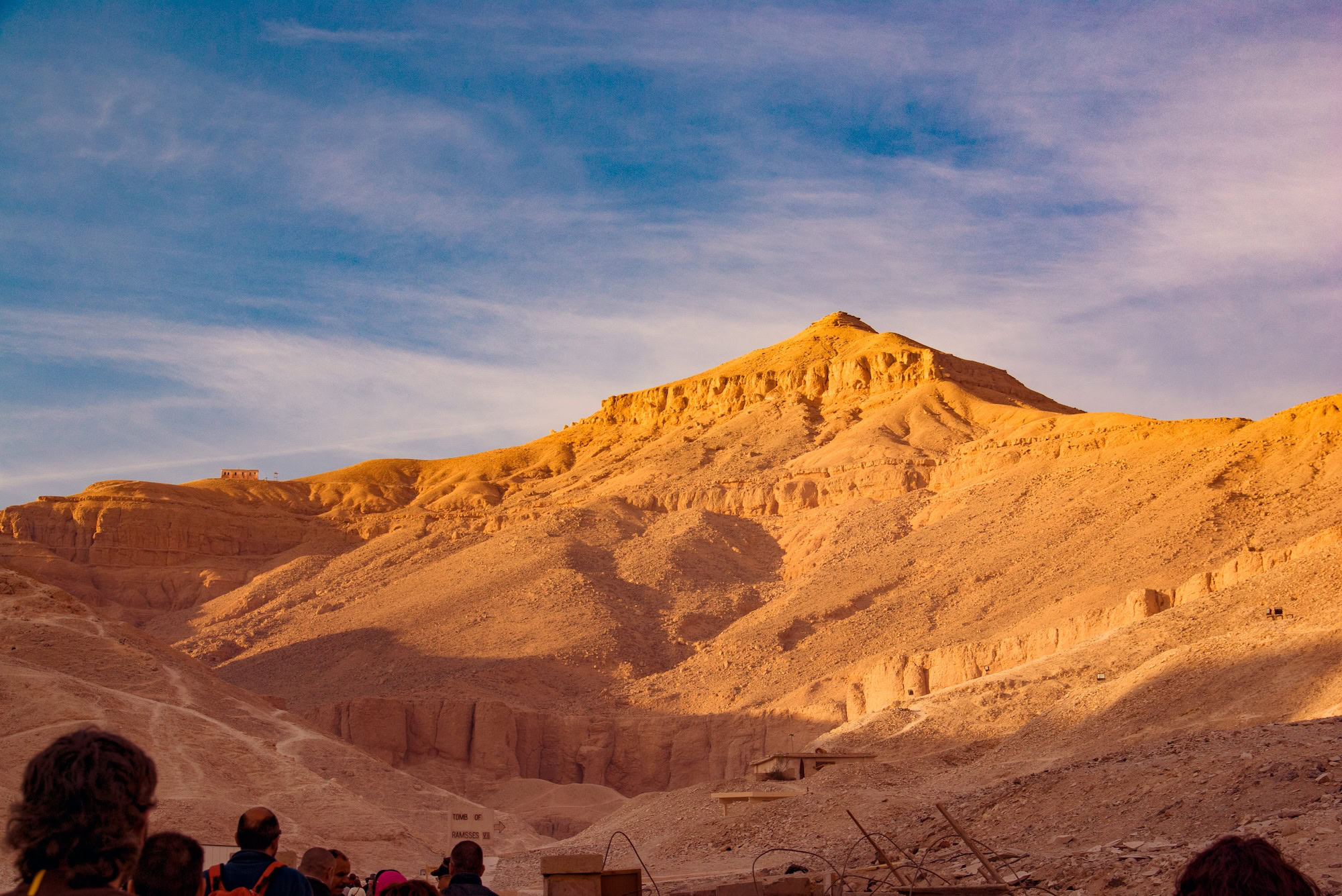 Tourists exploring the Valley of the Kings archaeological site with limestone cliffs and desert mountains