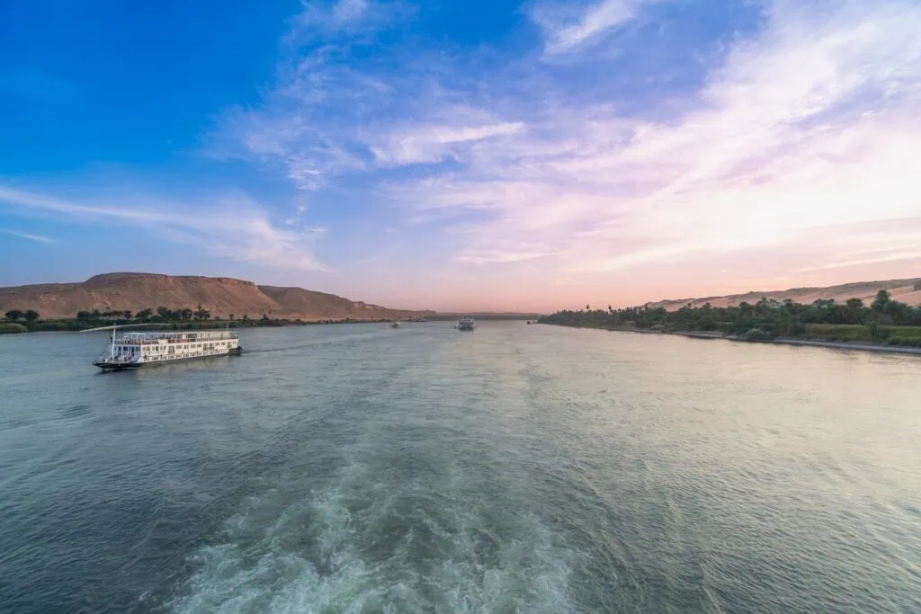 A traditional dahabiya sailing vessel on the calm Nile River at dusk near Esna, with soft colourful skies and distant desert banks, Egypt.
