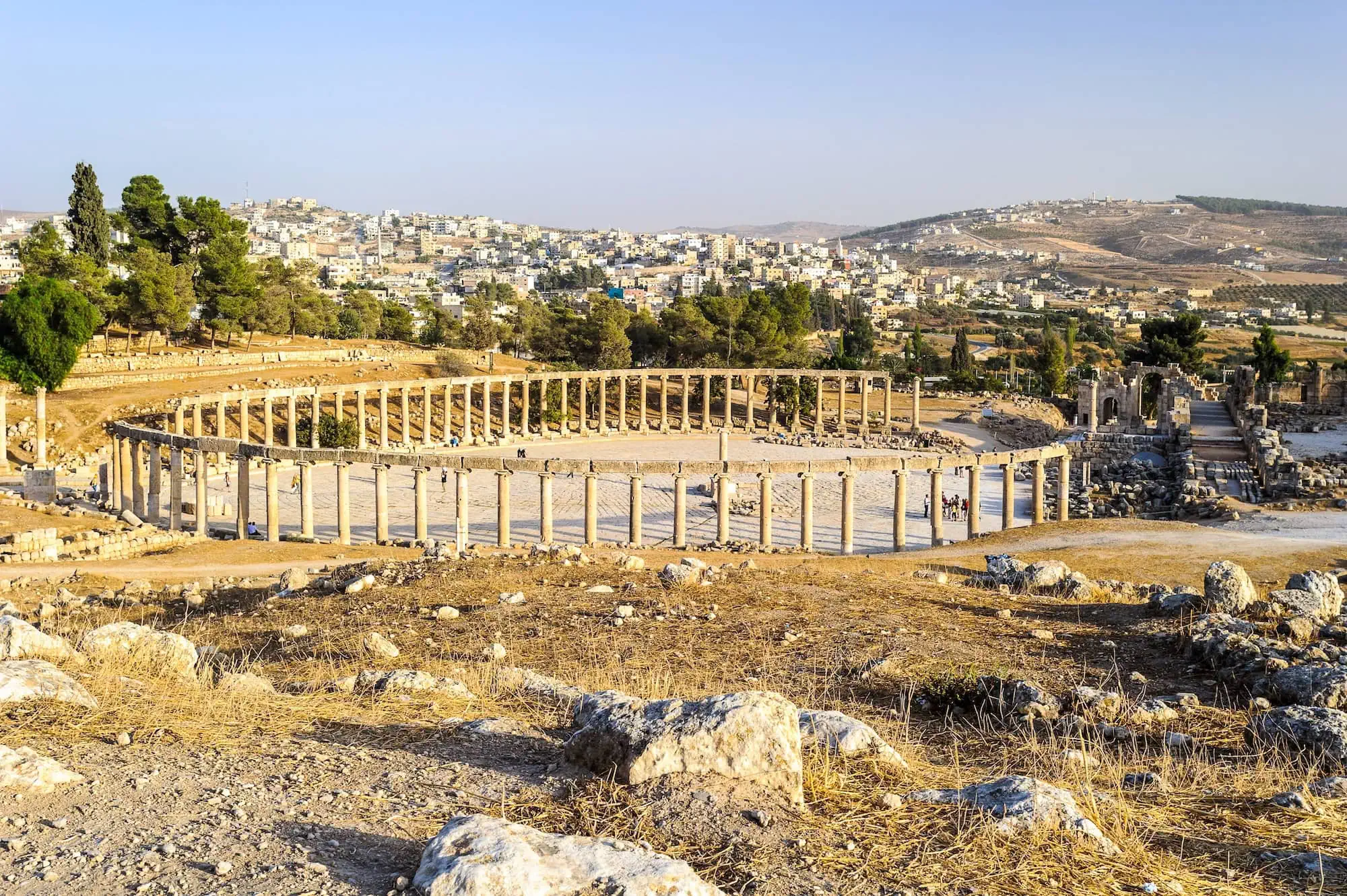Panoramic view of ancient Roman Oval Forum ruins in Jerash with modern Jordanian city in background