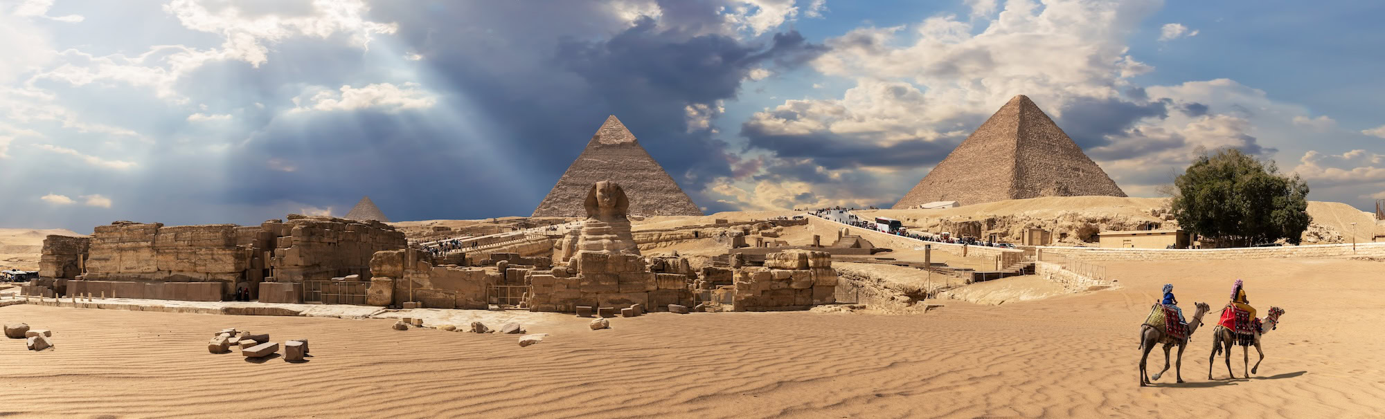 Giza Pyramids and Sphinx with camels and tourists in desert landscape