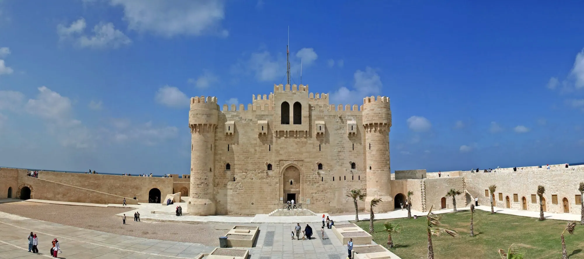 Qaitbay Citadel fortress in Alexandria with stone walls, towers, and tourists exploring the courtyard