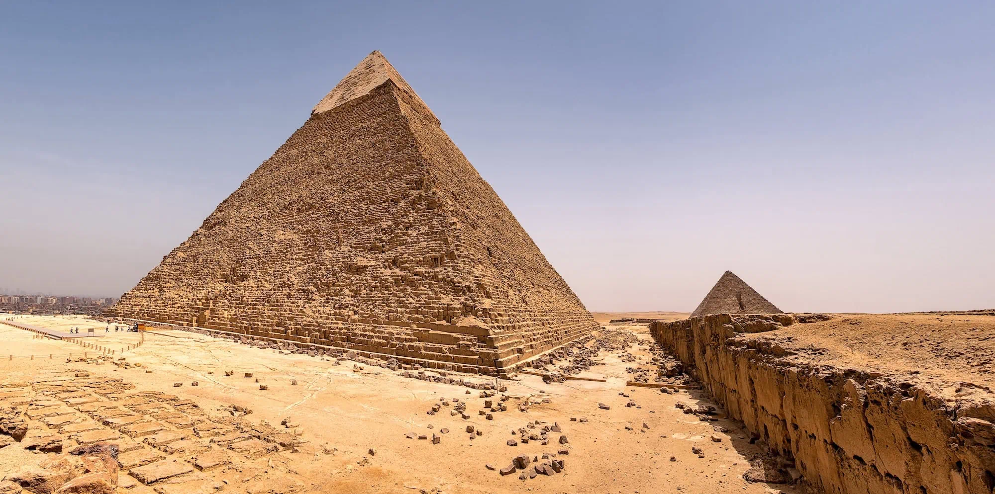 Tourists walking near the Great Pyramid of Giza entrance with ancient stone blocks visible