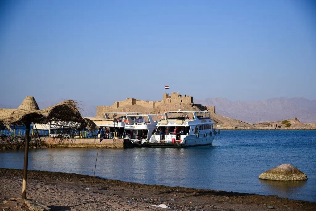 View of Salah El-Din Castle on Pharaoh’s Island with a sightseeing boat along the shoreline of the Sinai Peninsula, Taba