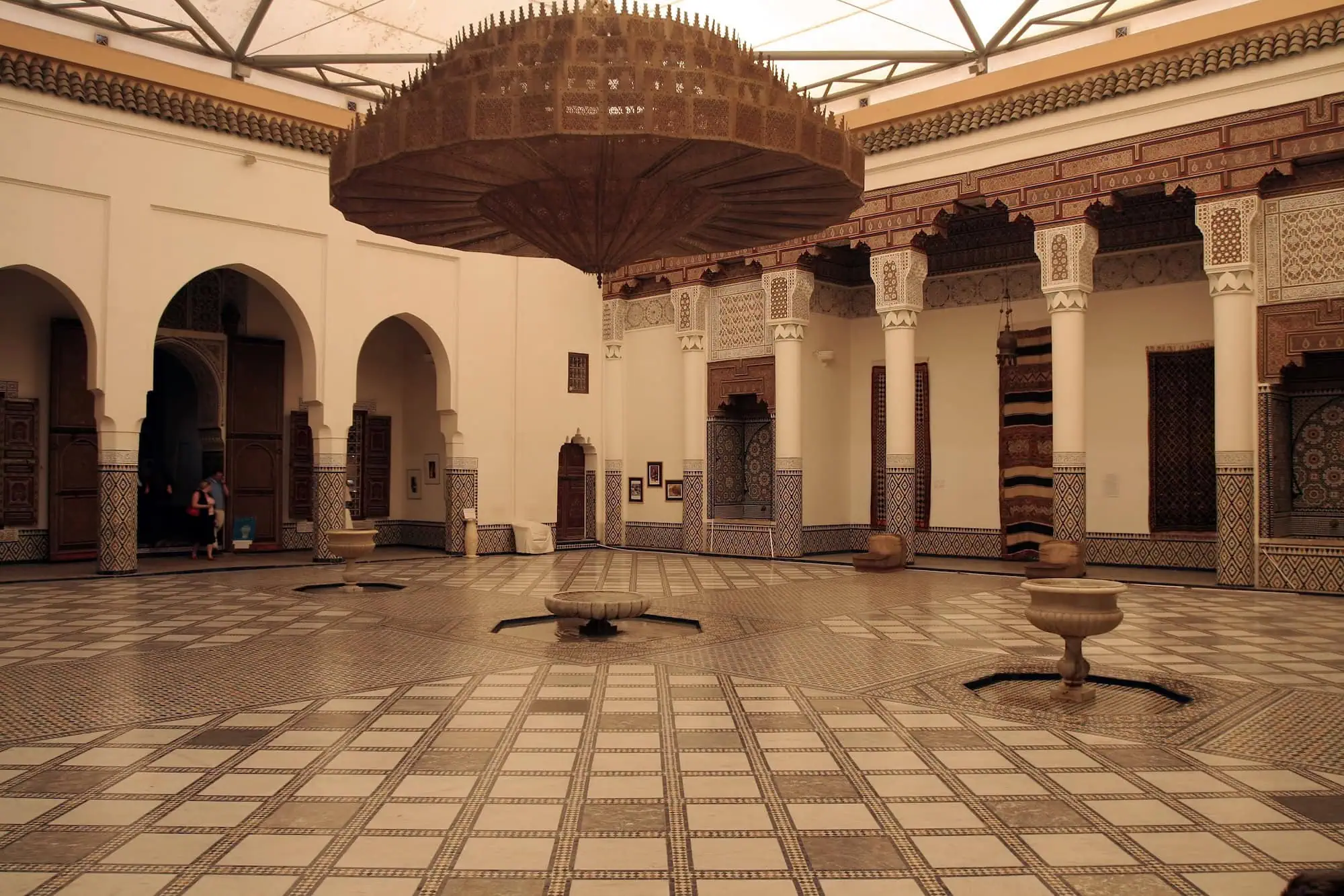 Traditional Moroccan palace interior featuring horseshoe arches, geometric tilework, ornate columns and carved wooden balconies