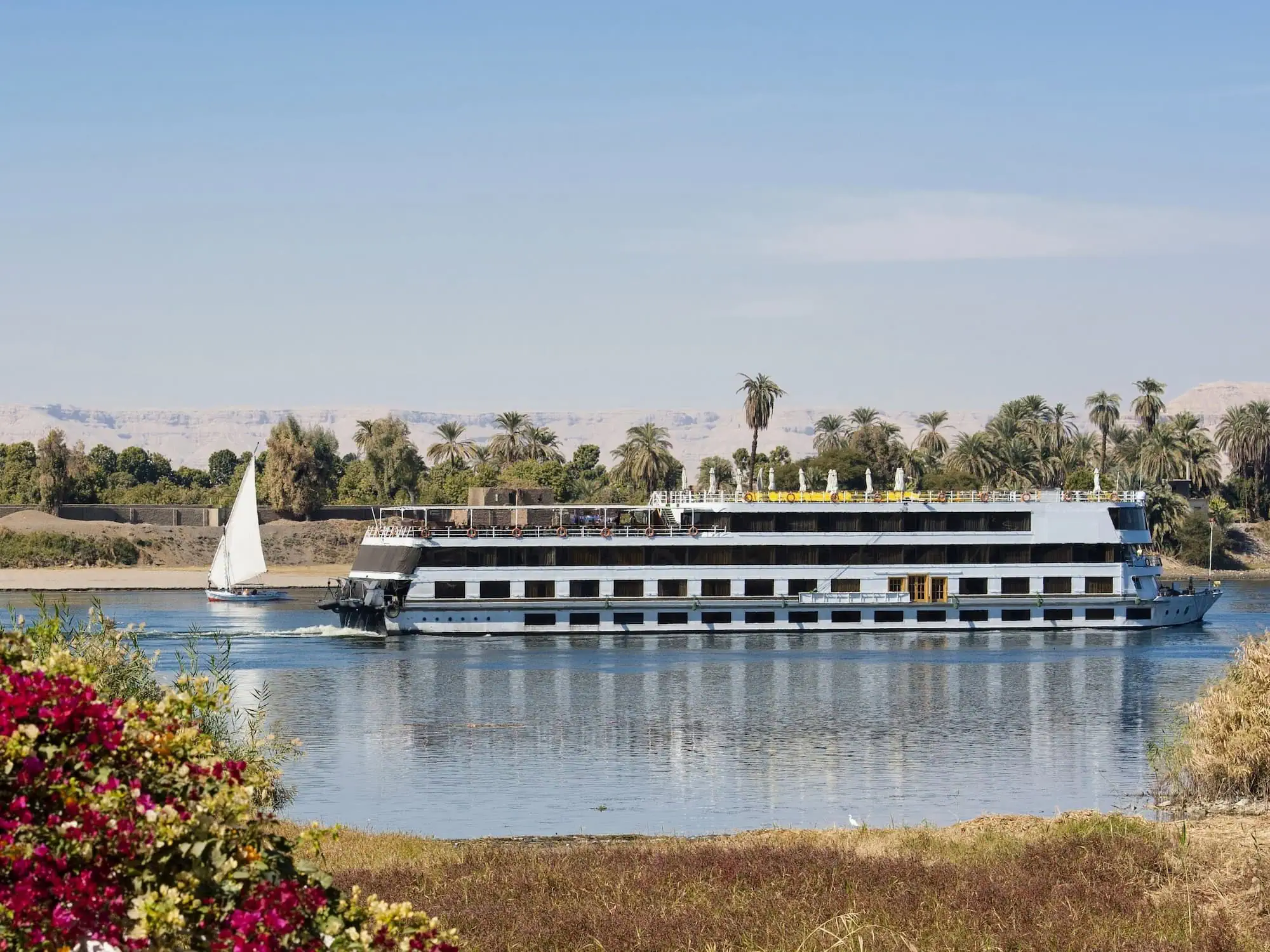 Multi-deck Luxury Nile Cruise vessel on the Nile River with a traditional Egyptian felucca sailing nearby, between Luxor and Aswan
