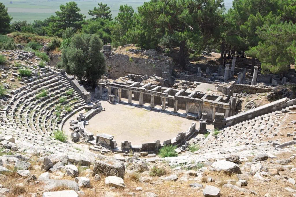 Semi-circular stone seating and stage remains on a slope at Priene Amphitheater, Aydın