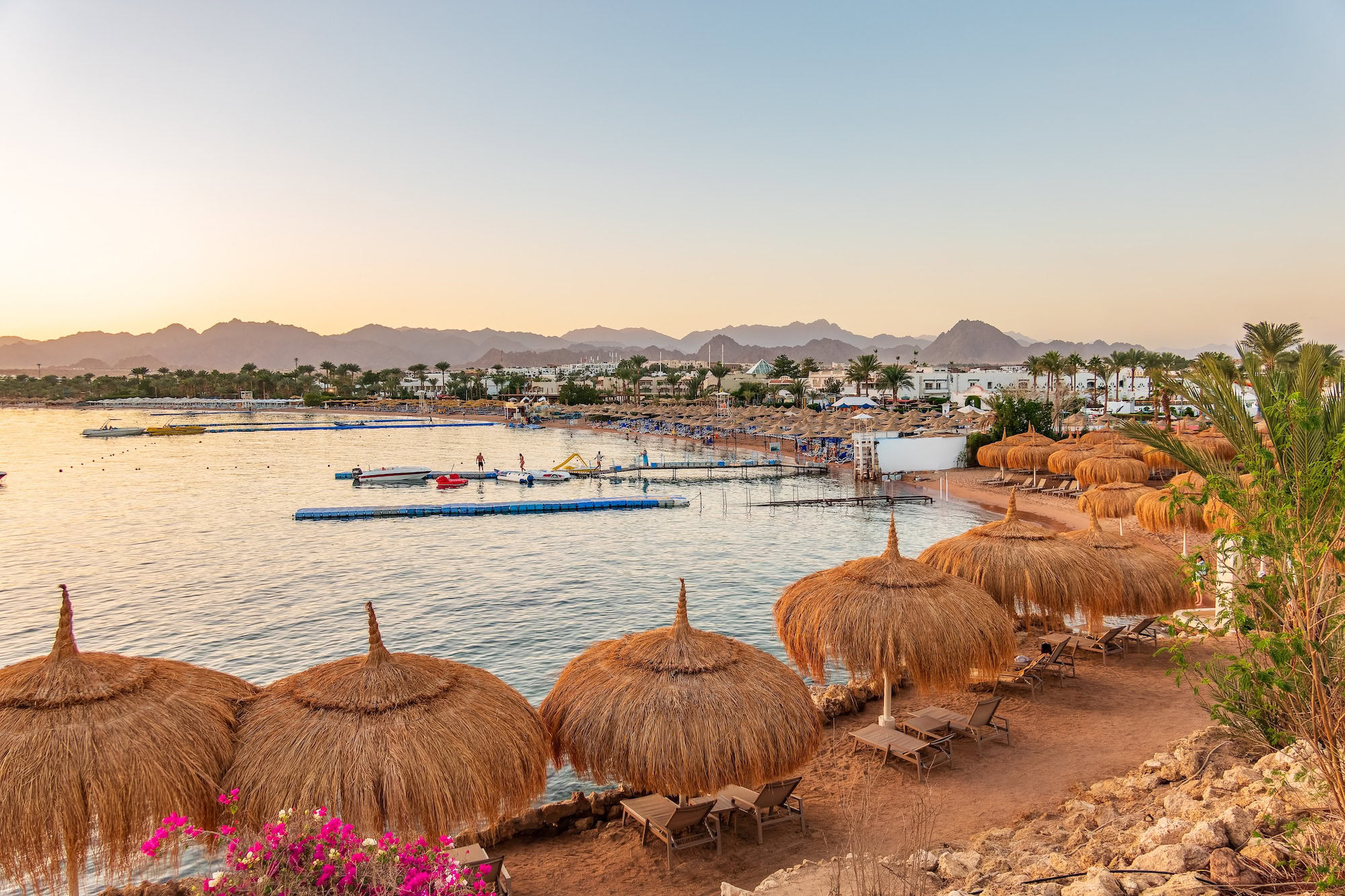 Red Sea beach resort with umbrellas, palm trees, boats and mountains in Egypt