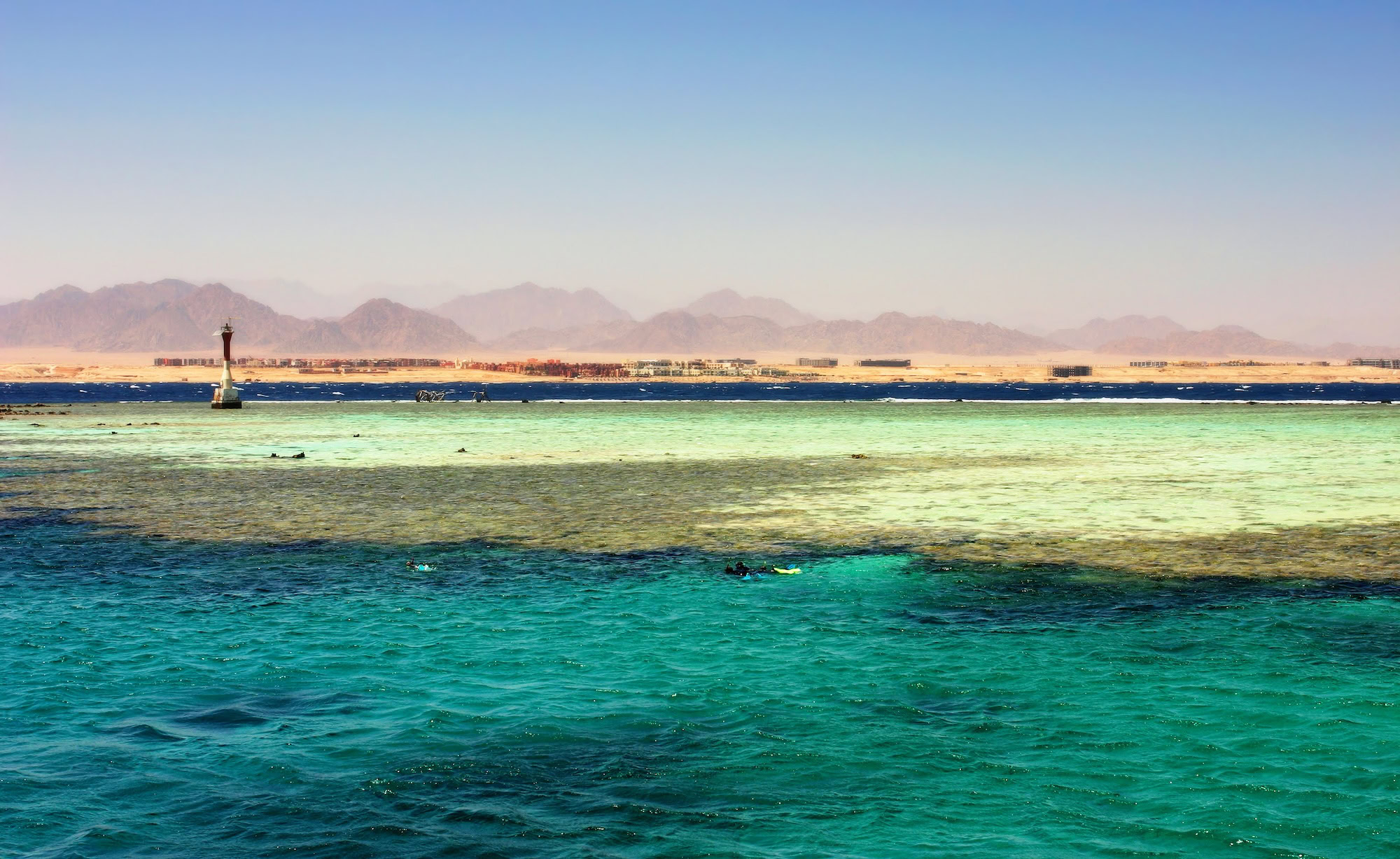 Red Sea coral reef with snorkelers and boats along desert coastline