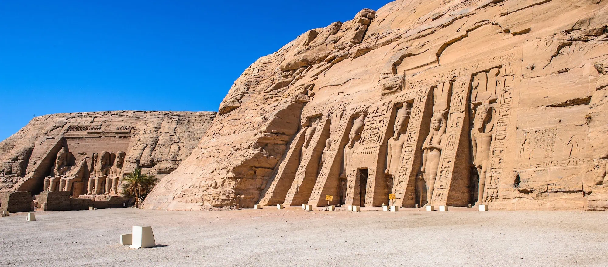 Two massive Abu Simbel temple facades carved into sandstone cliffs with colossal pharaoh statues