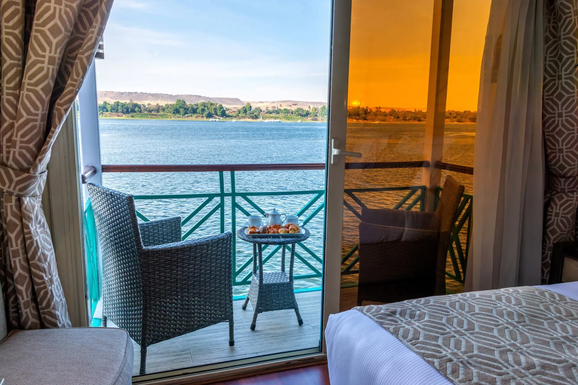 Interior view of a suite cabin with private balcony on a Luxury Nile Cruise vessel sailing the Luxor–Aswan route, with sliding glass doors opening onto a private outdoor deck overlooking the Nile