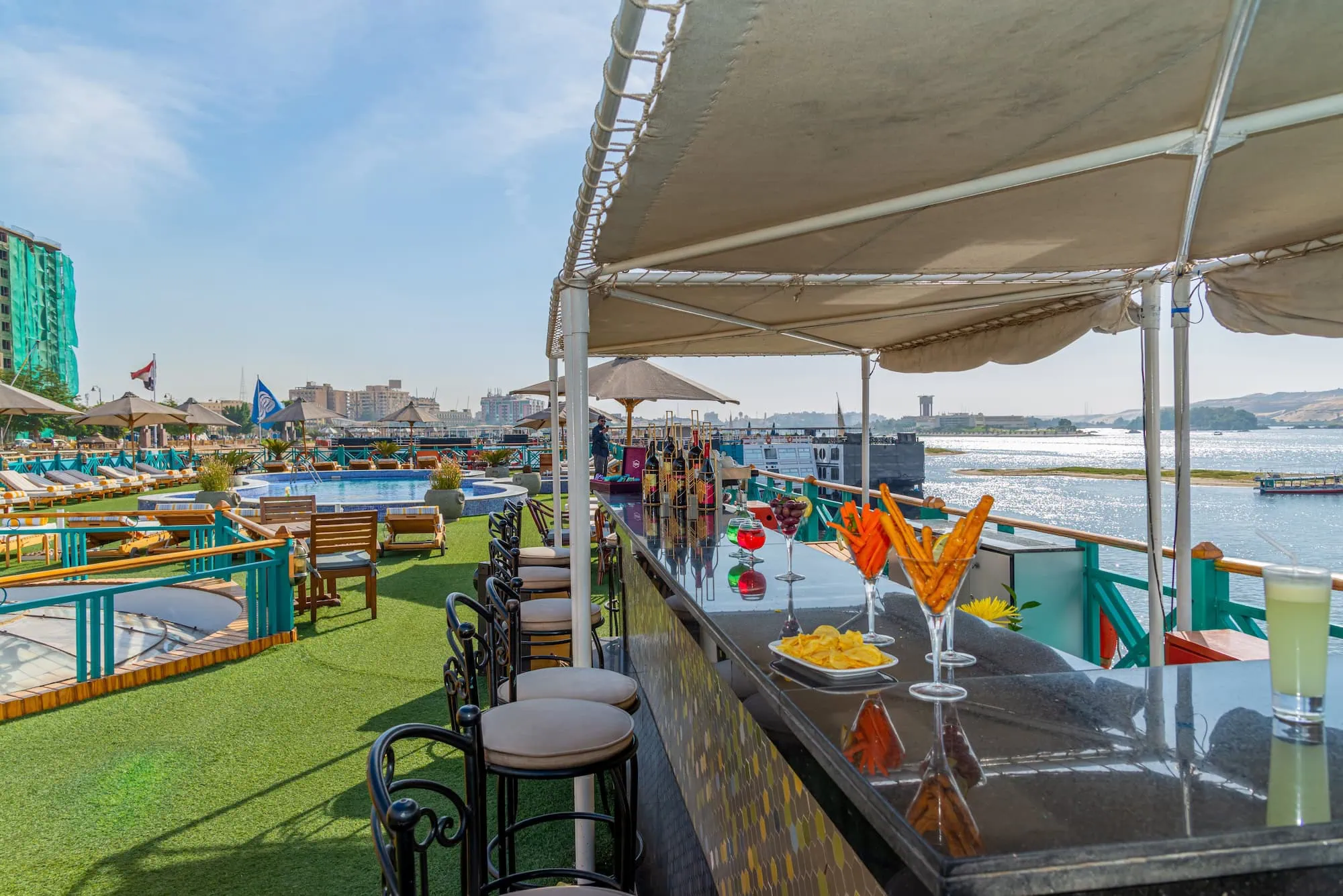 The sun deck of a Luxury Nile Cruise vessel with swimming pool, bar, and elegant lounge seating, sailing the Nile between Luxor and Aswan, Egypt.